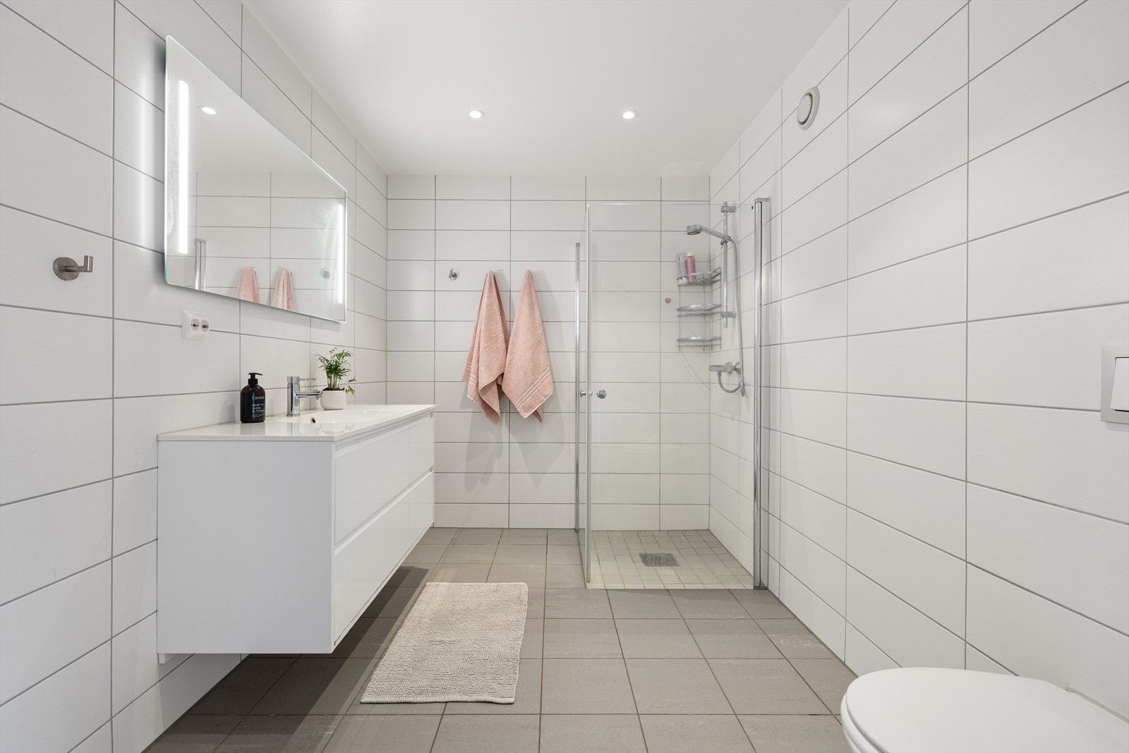 Flislagt baderom med behagelig varme i gulvet. Badet er innredet med vegghengt toalett, dusjhjørne med glassdører, baderomsinnredning med servant og blandebatteri og speil. Galleribilde