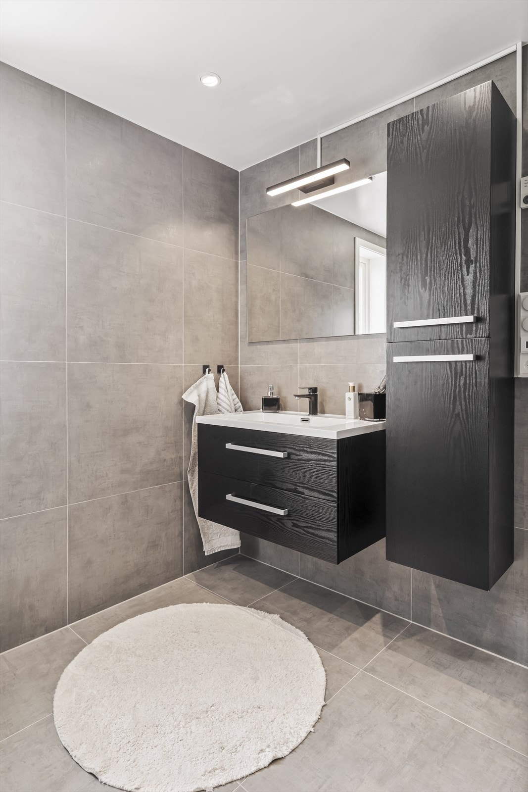 Badet er delikat innredet med store, grå fliser på gulv og vegger. Galleribilde
