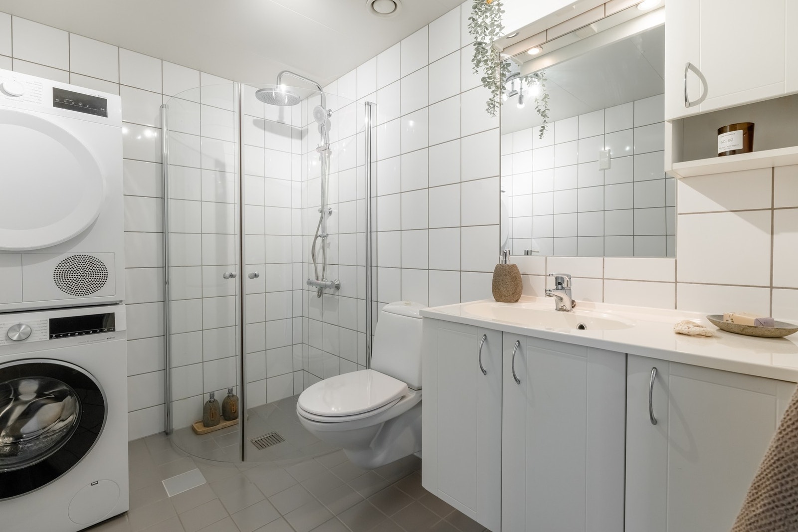 Badet har en stilren innredning med skap, ovenpåliggende servant og speil med belysning over. Videre er det vegghengt toalett og regnfallsdusj med innfellbare dusjdører. Galleribilde