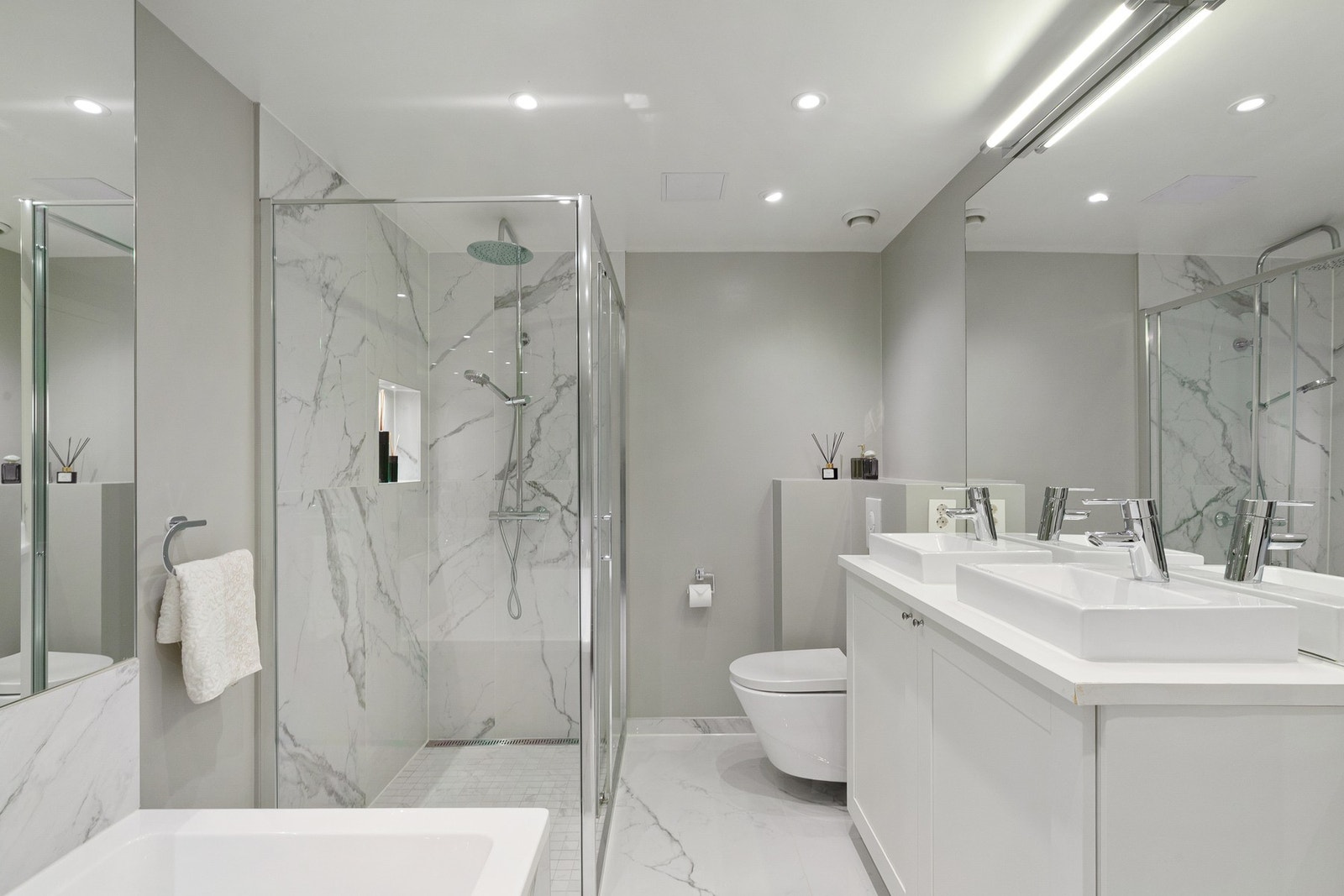 Bad med badekar, dusj og dobbelservant. Badet har marmor-inspirerte keramiske fliser, Statuario Plus i storformatet 60x120, med mosaikk på gulv i dusjen. Galleribilde