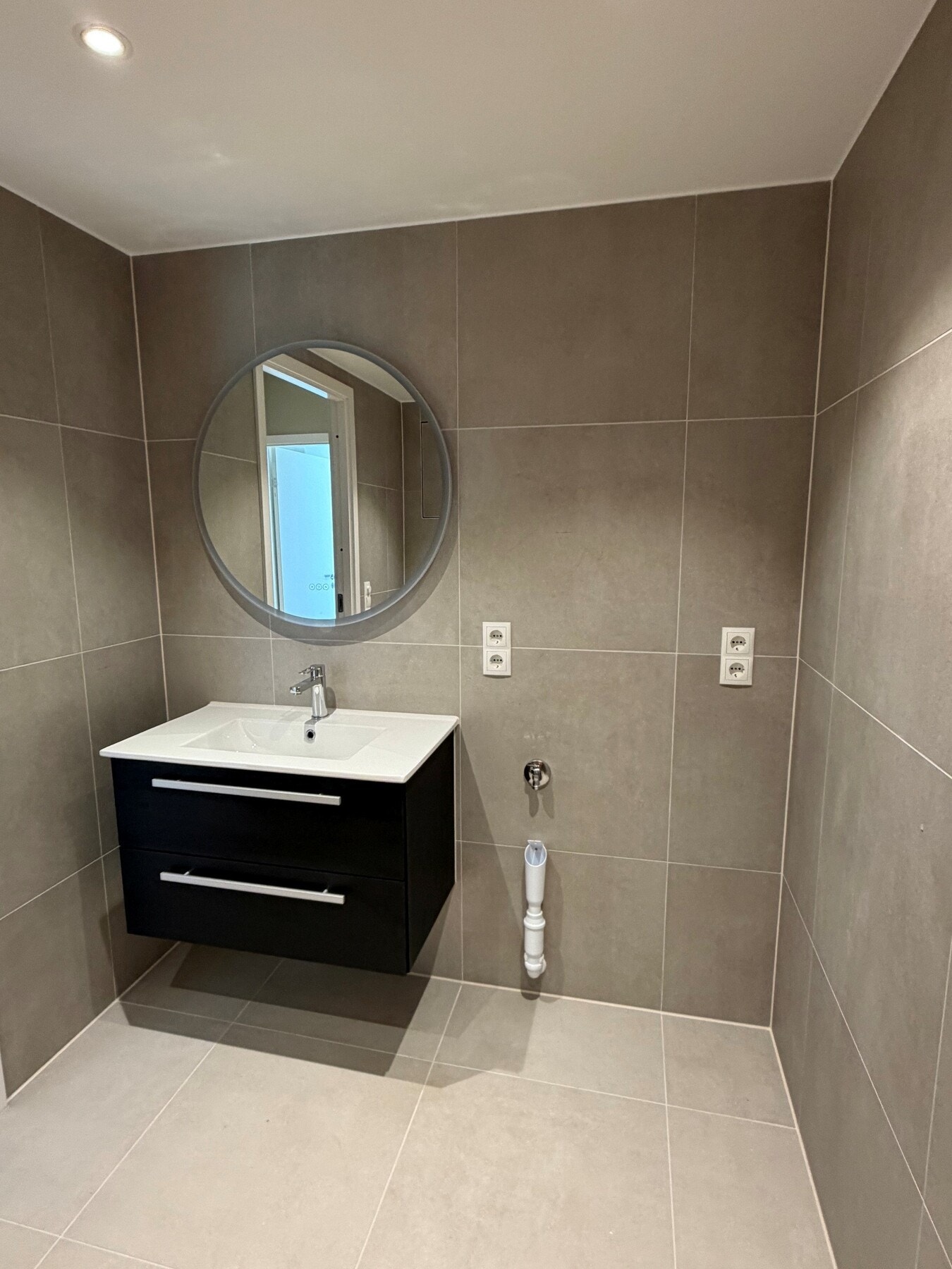 Badet får et moderne og stilrent preg med store grå fliser på både gulv og vegger, kombinert med et nedsenket mosaikkfelt i dusjsonen (5x5 cm). Galleribilde