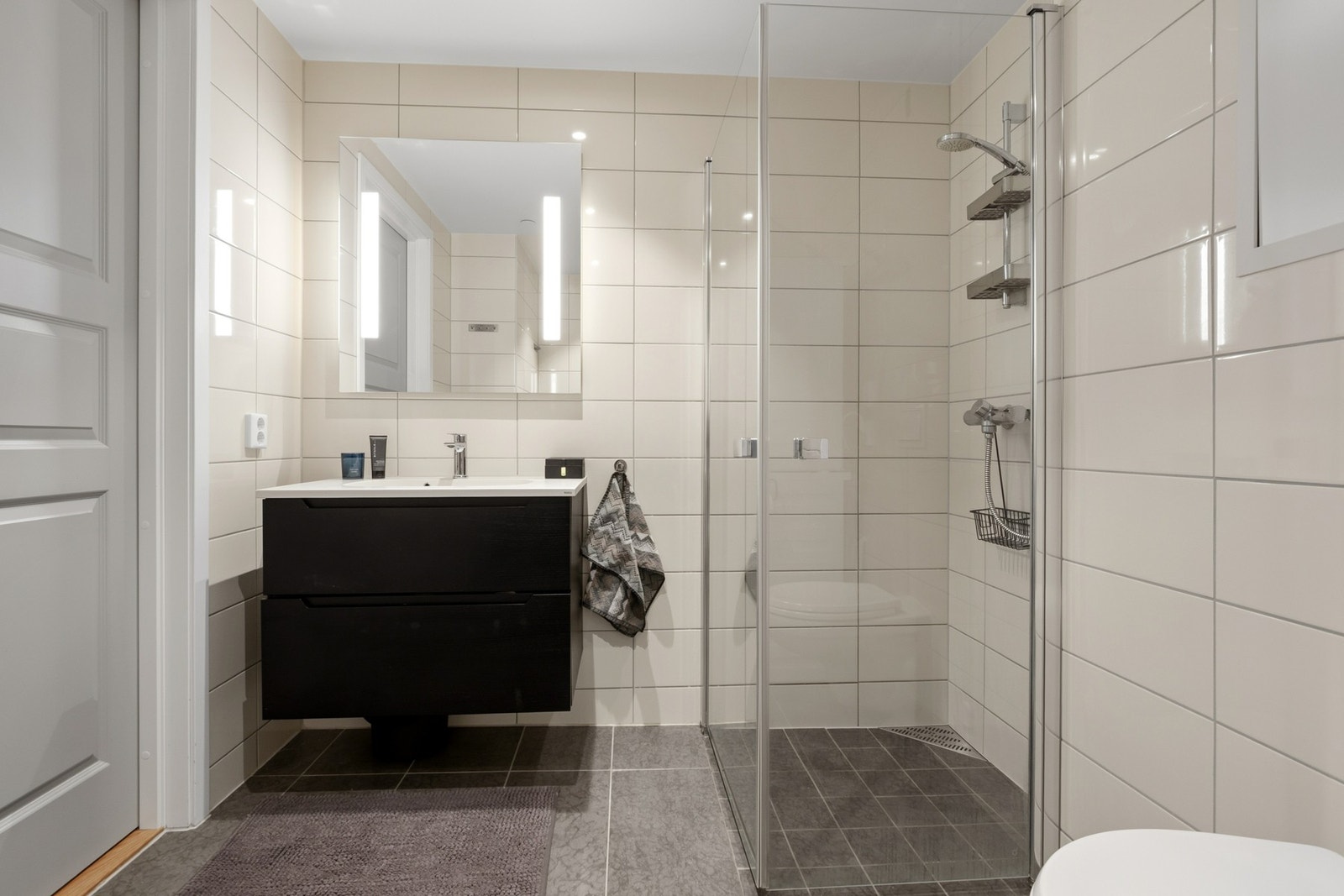 Badet fremstår som velholdt og pent, med lyse fliser på veggene, downlights i himlingen og grå fliser på gulv med gulvvarme. Galleribilde