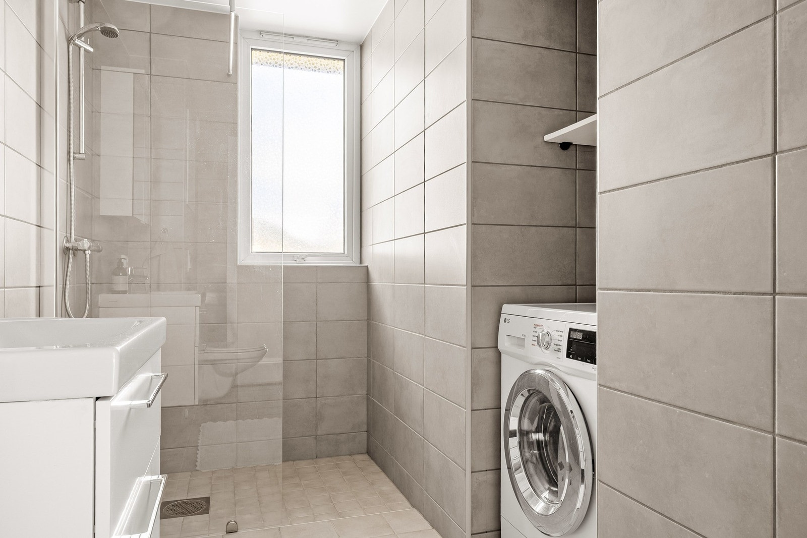 Badet er innredet med vegghengt toalett, servant med innredning, dusj med glassvegg og opplegg for vaskemaskin. Galleribilde