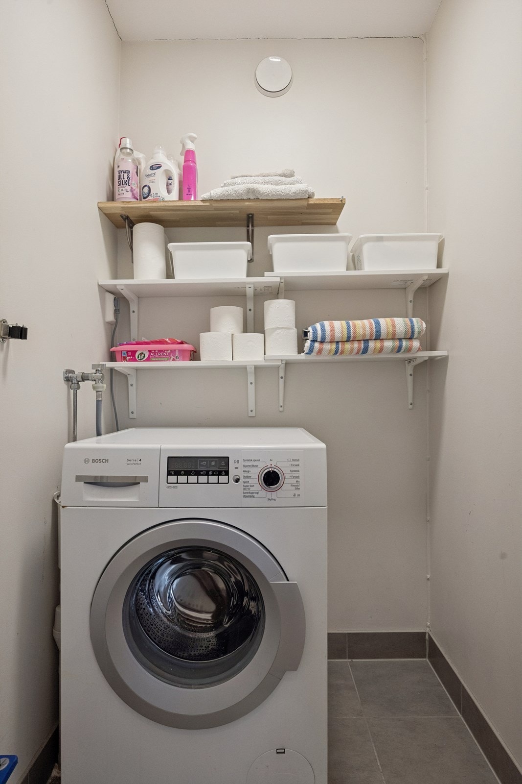 Leiligheten har også et separat vaskerom med flislagt gulv, sluk, opplegg for vaskemaskin og hyller til lagring. Galleribilde