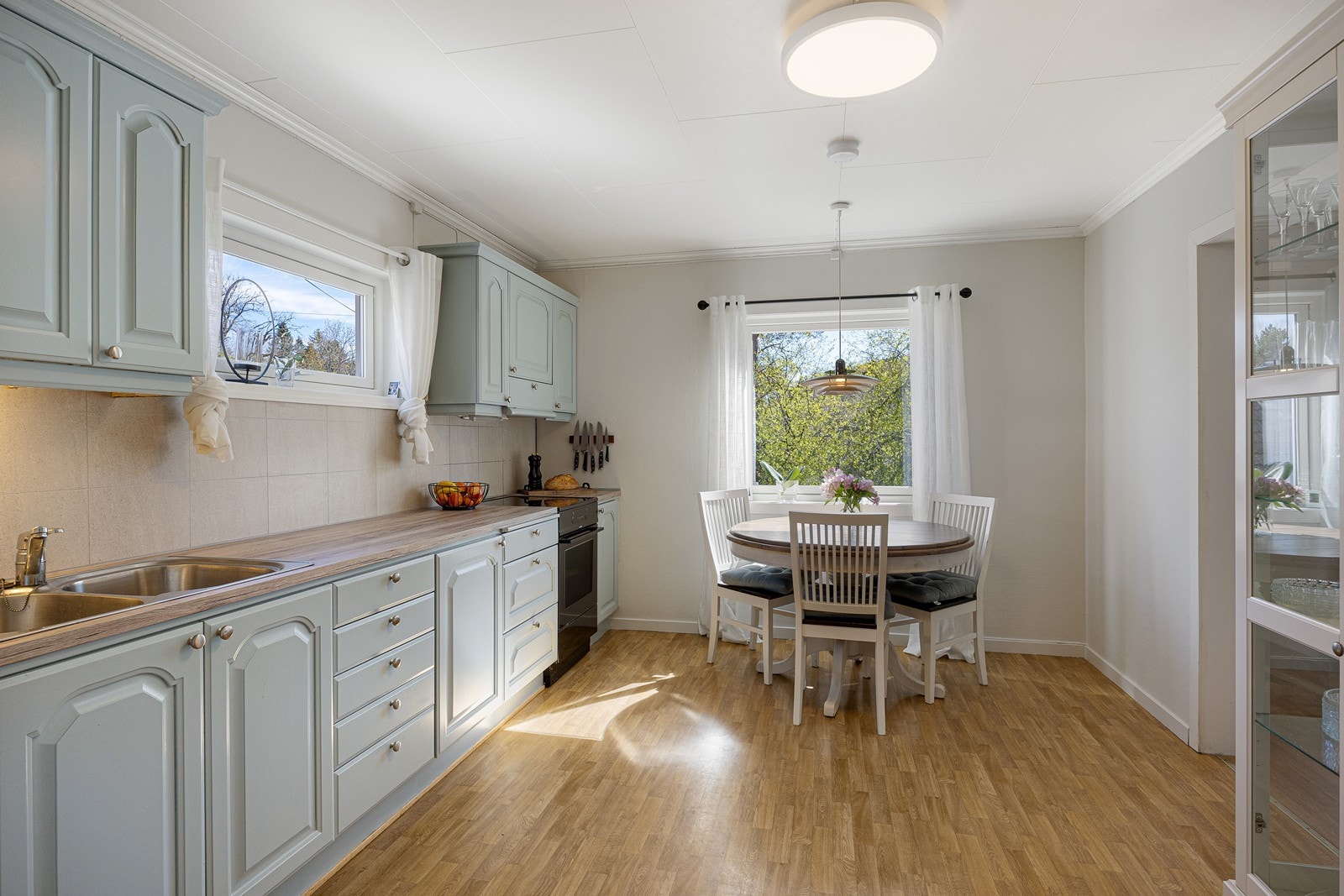Kjøkkenet har et klassisk og pent design med gode benkeflater og rikelig med oppbevaringsplass. Innredningen har lysmalte, profilerte fronter og pent laminatbenkeplate med nedfelt, dobbel oppvaskkum. Galleribilde
