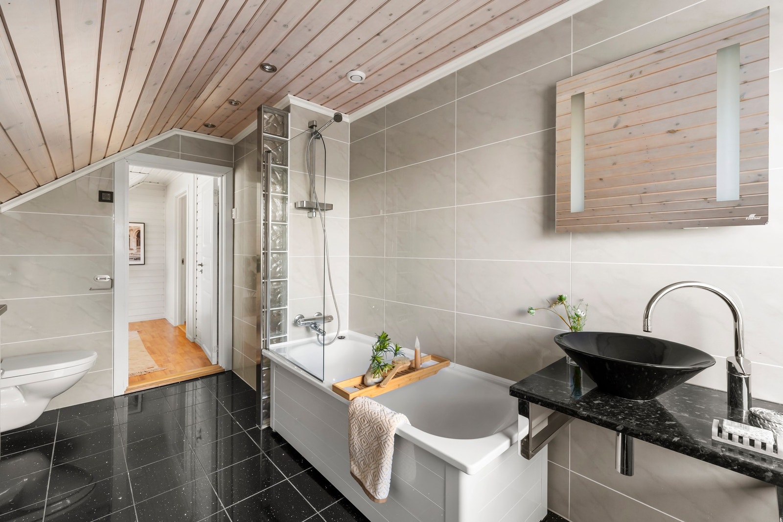 Badet byr på skapinnredning, moderne servantløsning, vegghengt toalett og dusj i badekar med glassvegg. Galleribilde