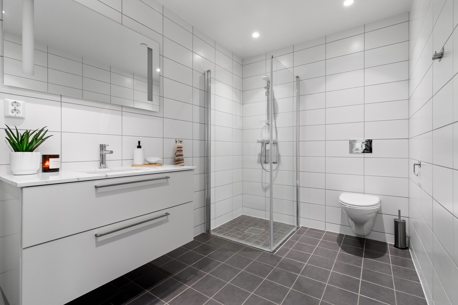 Badet er stilrent og pent, med fliser på vegger og gulv. Badet er innredet med vegghengt servant- og speilskap, toalett og dusjhjørne. Galleribilde