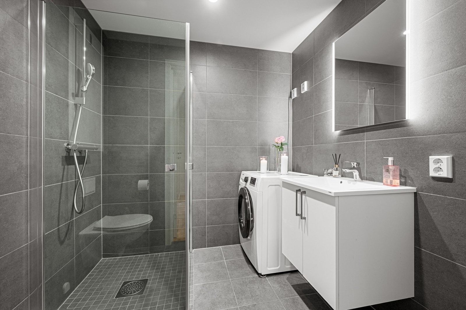 Badet er innredet med servantinnredning, speil med integrert belysning, veggmontert toalett, og dusjhjørne. Det er også opplegg for vaskemaskin. Galleribilde