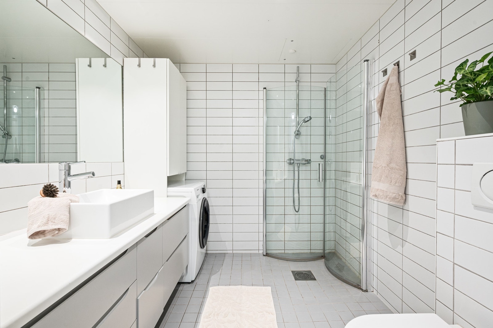 Badet er pent flislagt på gulv og vegger med varme i gulvet. Baderomsinnredningen består av vegghengt servantinnredning med servant. Opplegg for vaskemaskin. Galleribilde