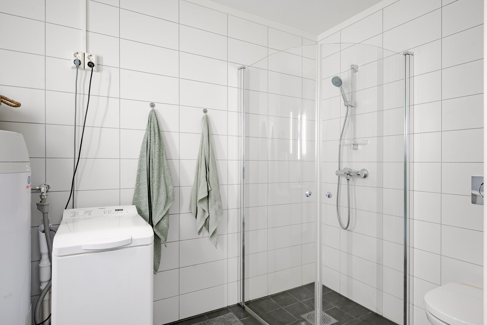 Leiligheten har et lyst og moderne baderom fra byggeåret 2022. Baderommet har mørke fliser på gulv, vannbåren gulvvarme, hvite fliser på veggene og avtrekk via balansert ventilasjon. Galleribilde