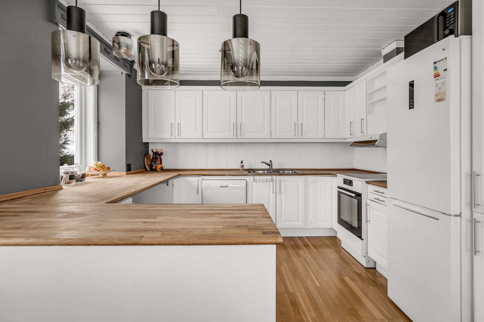 Lyst og koselig kjøkken med innredning med profilerte fronter og benkeplate av tre med nedfelt oppvaskkum. Kjøleskap, komfyr og oppvaskmaskin. Galleribilde