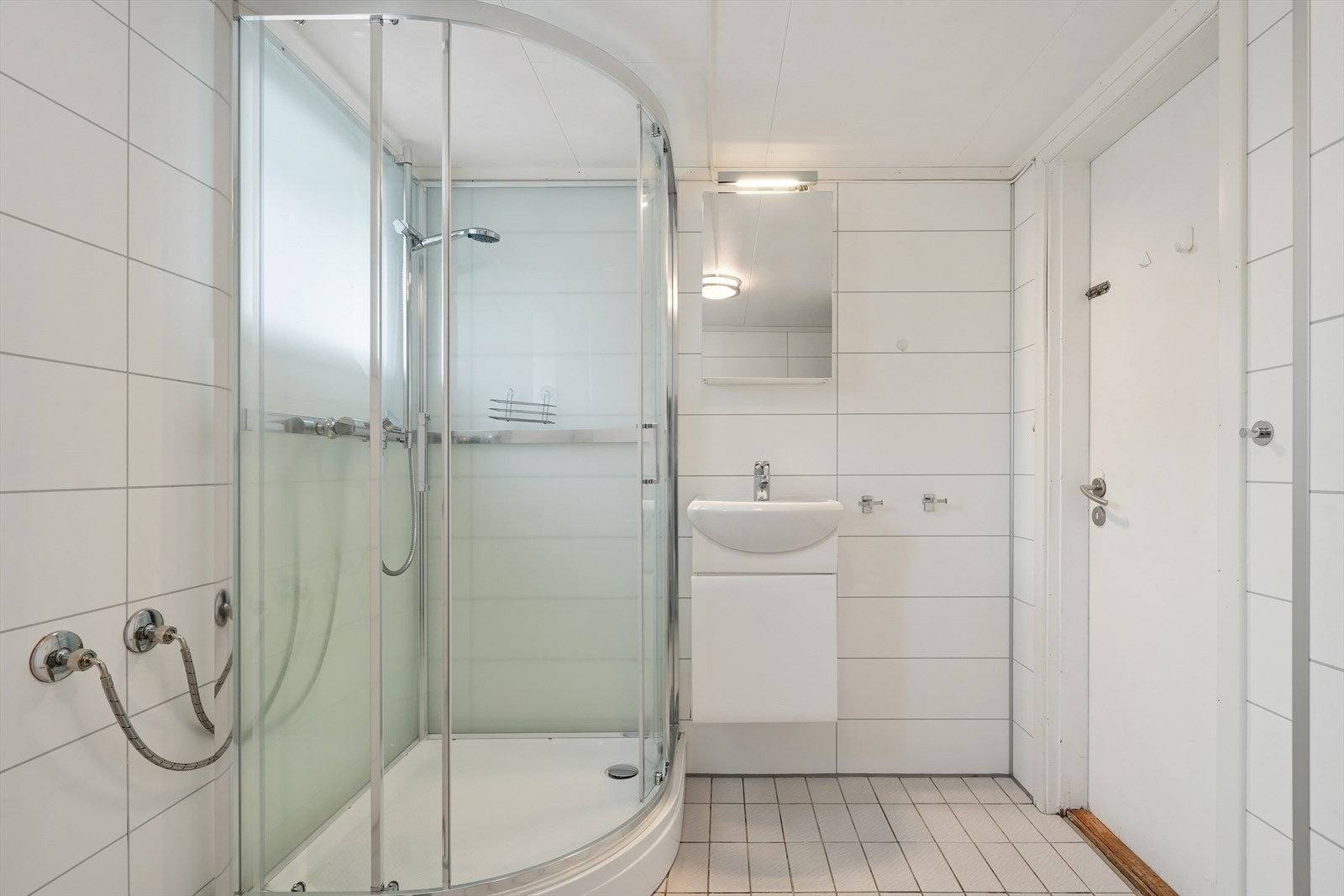 Bad/vaskerom i underetasjen med fliser på gulv, dusjkabinett, veggmontert toalett og opplegg for vaskemaskin. Galleribilde