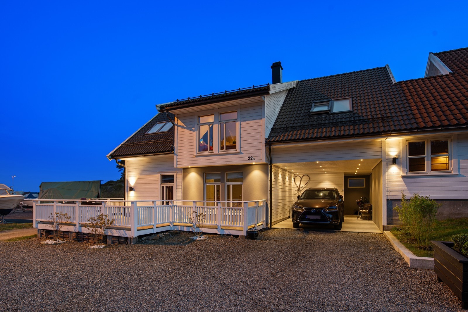 Innbydende fasade med carport, romslig terrasse og stemningsfull utebelysning som skaper en hyggelig atmosfære Galleribilde