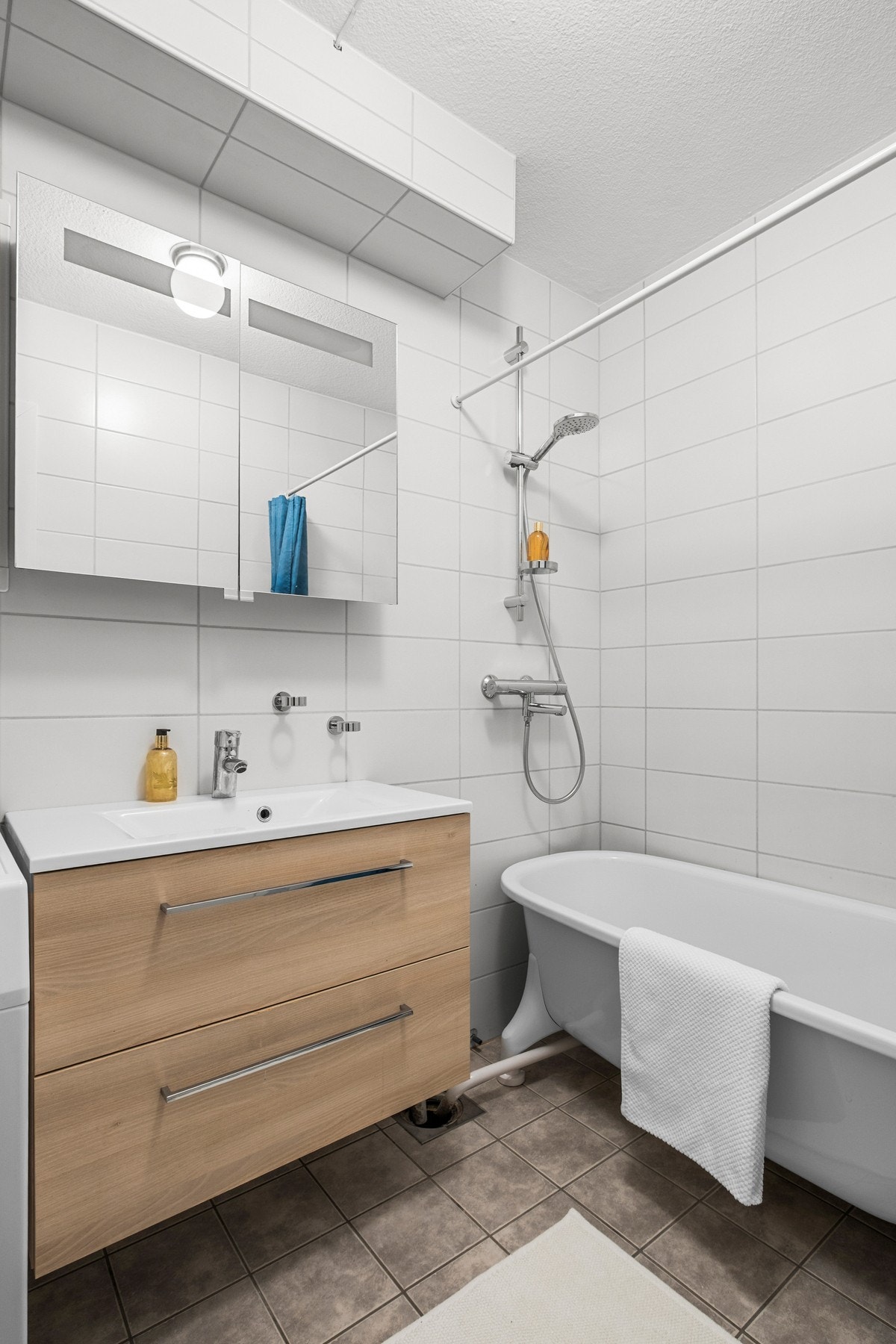 Badet er innredet med veggmontert servant og skapinnredning, speilskap med integrert belysning og dusjhjørne med badekar Galleribilde
