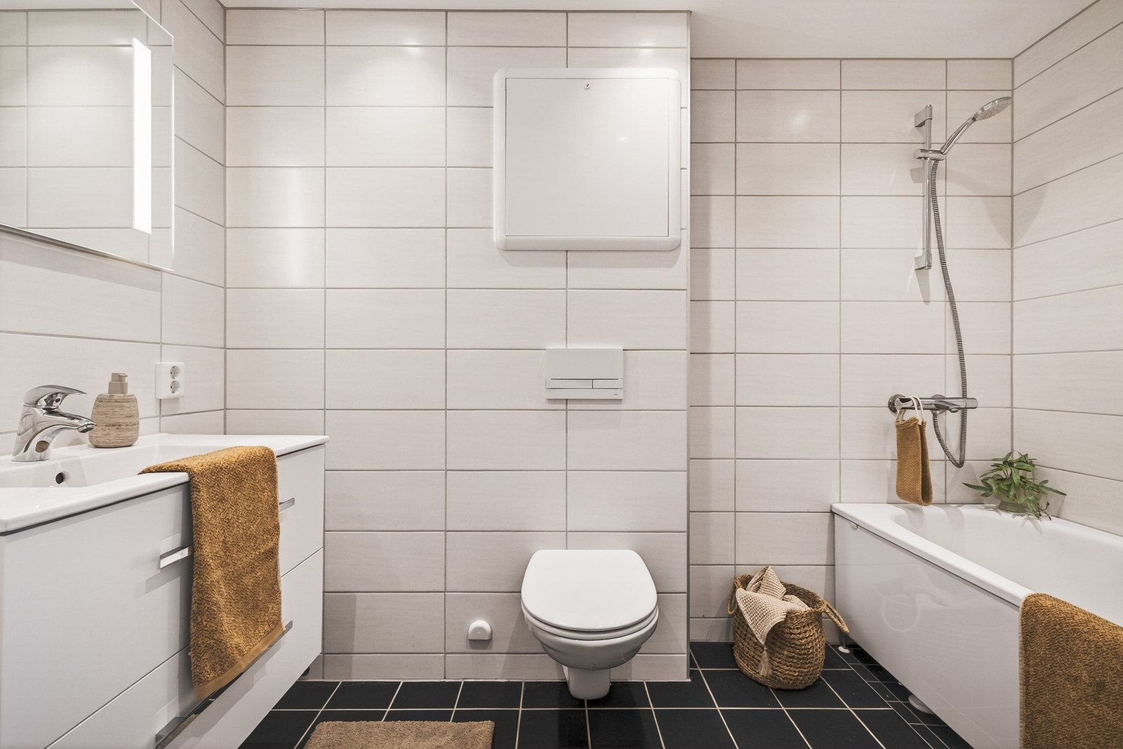 Badet er flislagt og har en praktisk og moderne innredning med badekar, vegghengt toalett og servant med tilhørende innredning. Galleribilde