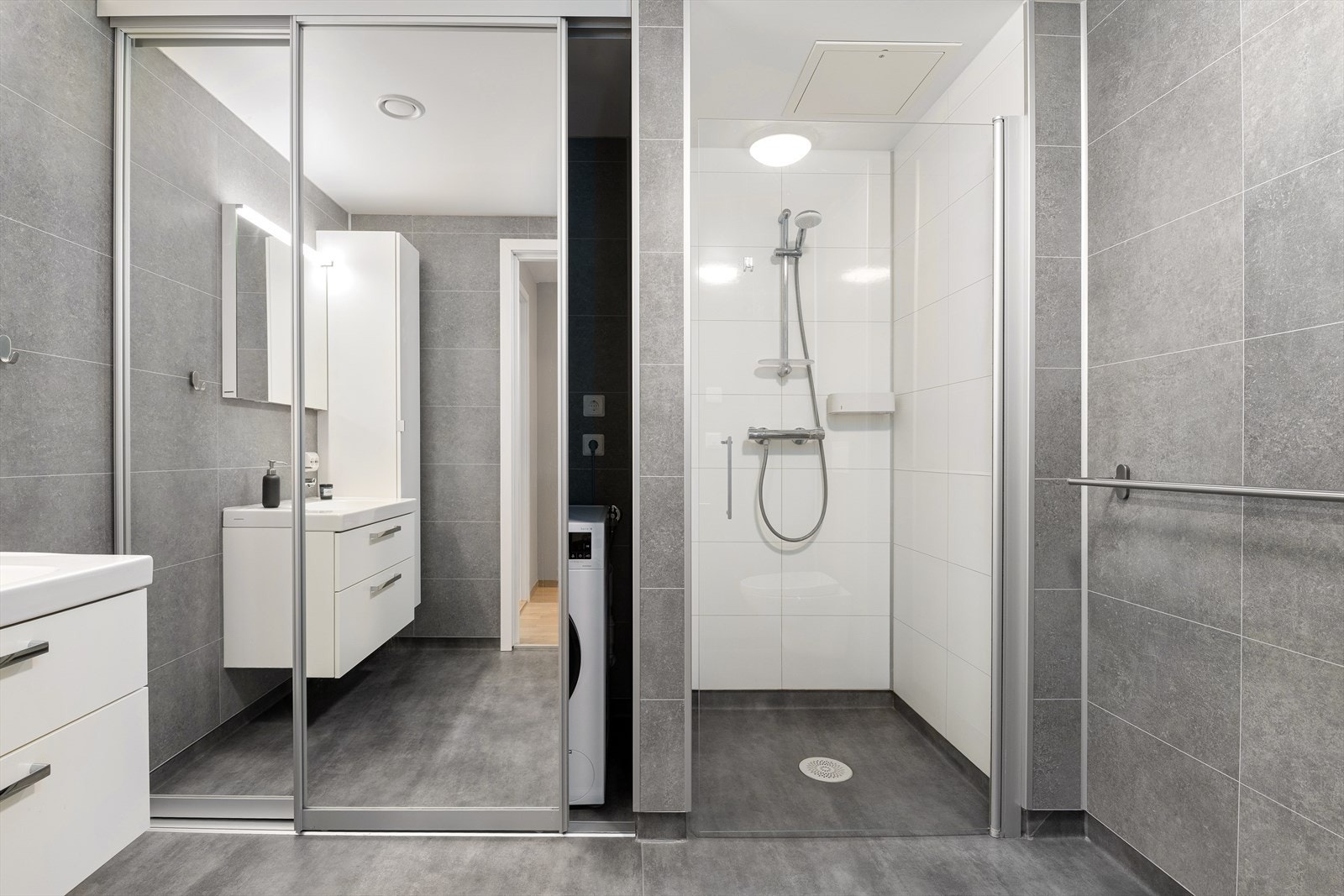Badet er innredet med dusjnisje, vegghengt toalett, høyskap, servant i innredninig med skufferr, samt opplegg for vaskemaskin og tørketrommel bak skyvedører. Galleribilde