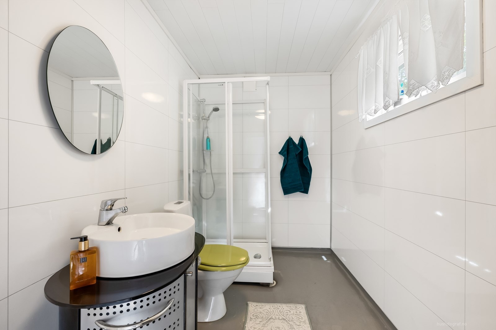 Delikat flislagt bad med vinylbelegg på gulv. Badet er innredet med bolle servant med rom for oppbevaring i skap, speil, toalett og dusjkabinett. Galleribilde
