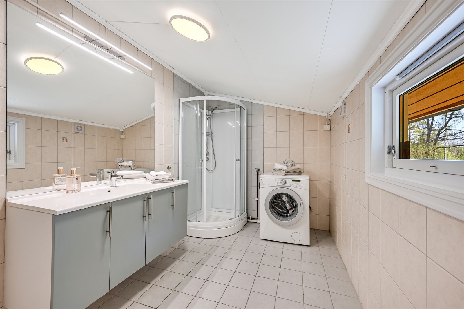 Badet har flislagte gulv og vegger og er innredet med dusjkabinett, servant i baderomsinnredningen, samt opplegg for vaskemaskin Galleribilde