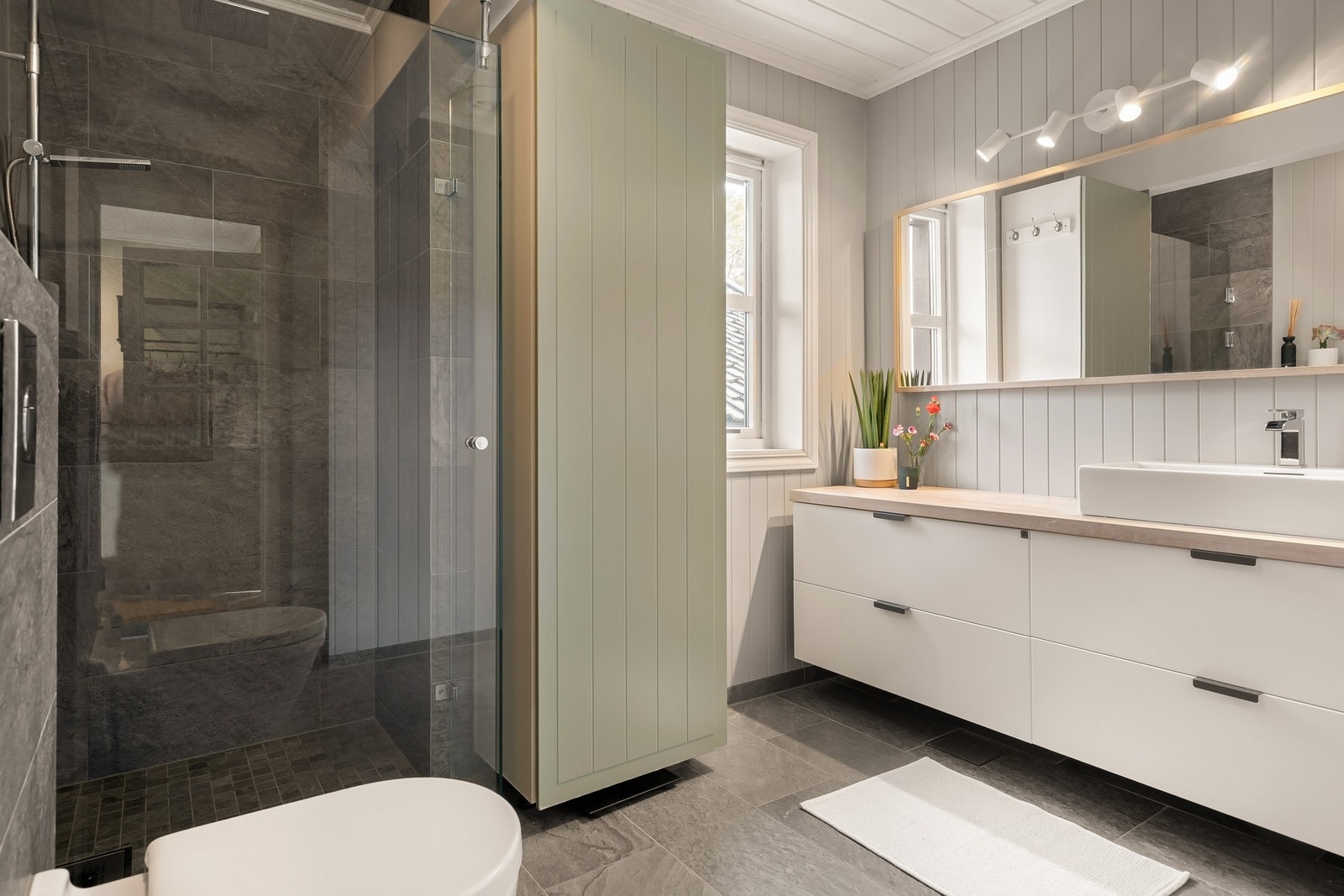 Badet har flislagt gulv med varmekabler, dusjnisje, vegghengt toalett og servantinnredning Galleribilde