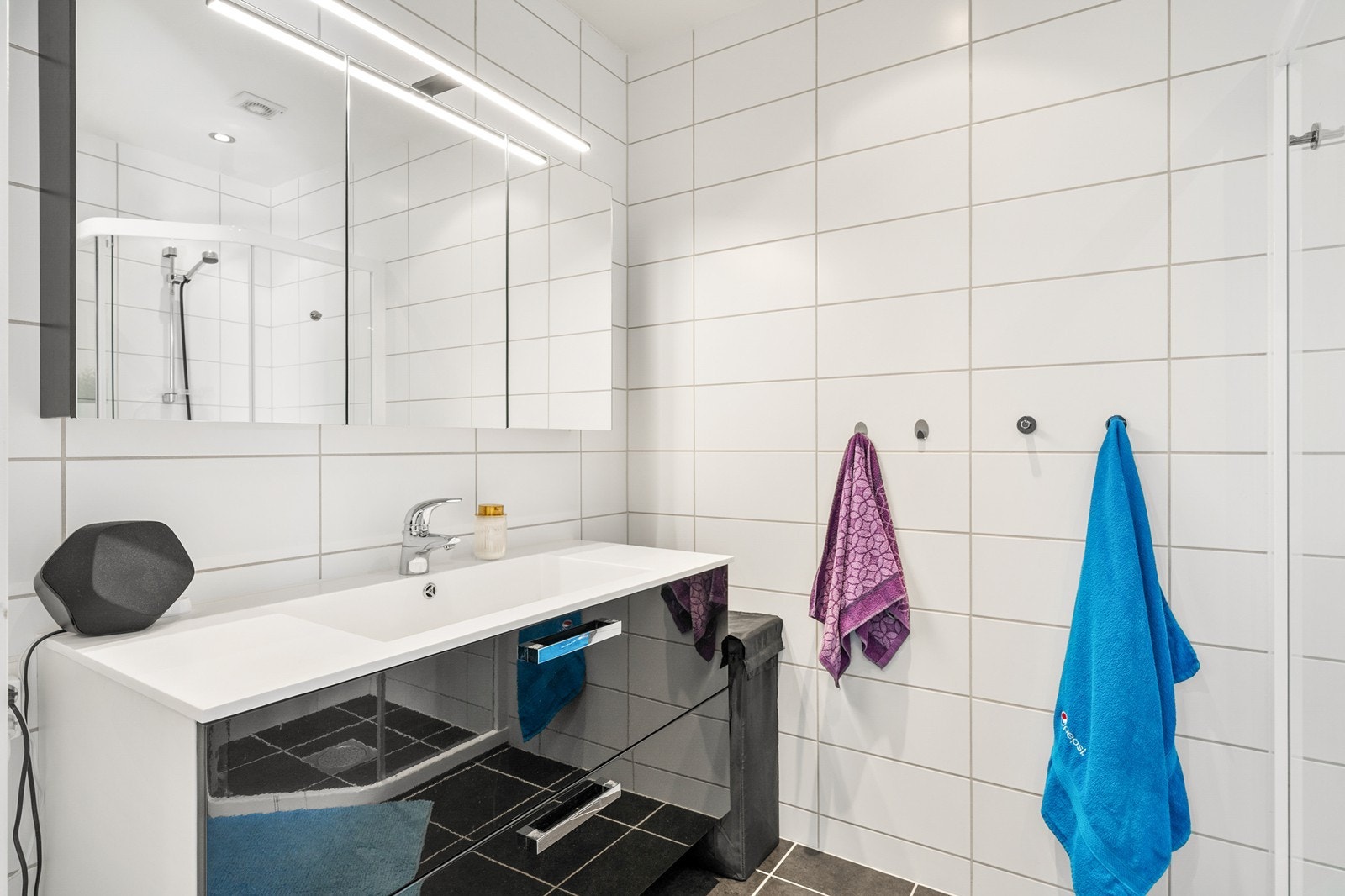 Badet er helfliset og har varmekabler i gulv. Badet er innredet med servant og speil, vegghengt toalett og dusjhjørne. Galleribilde