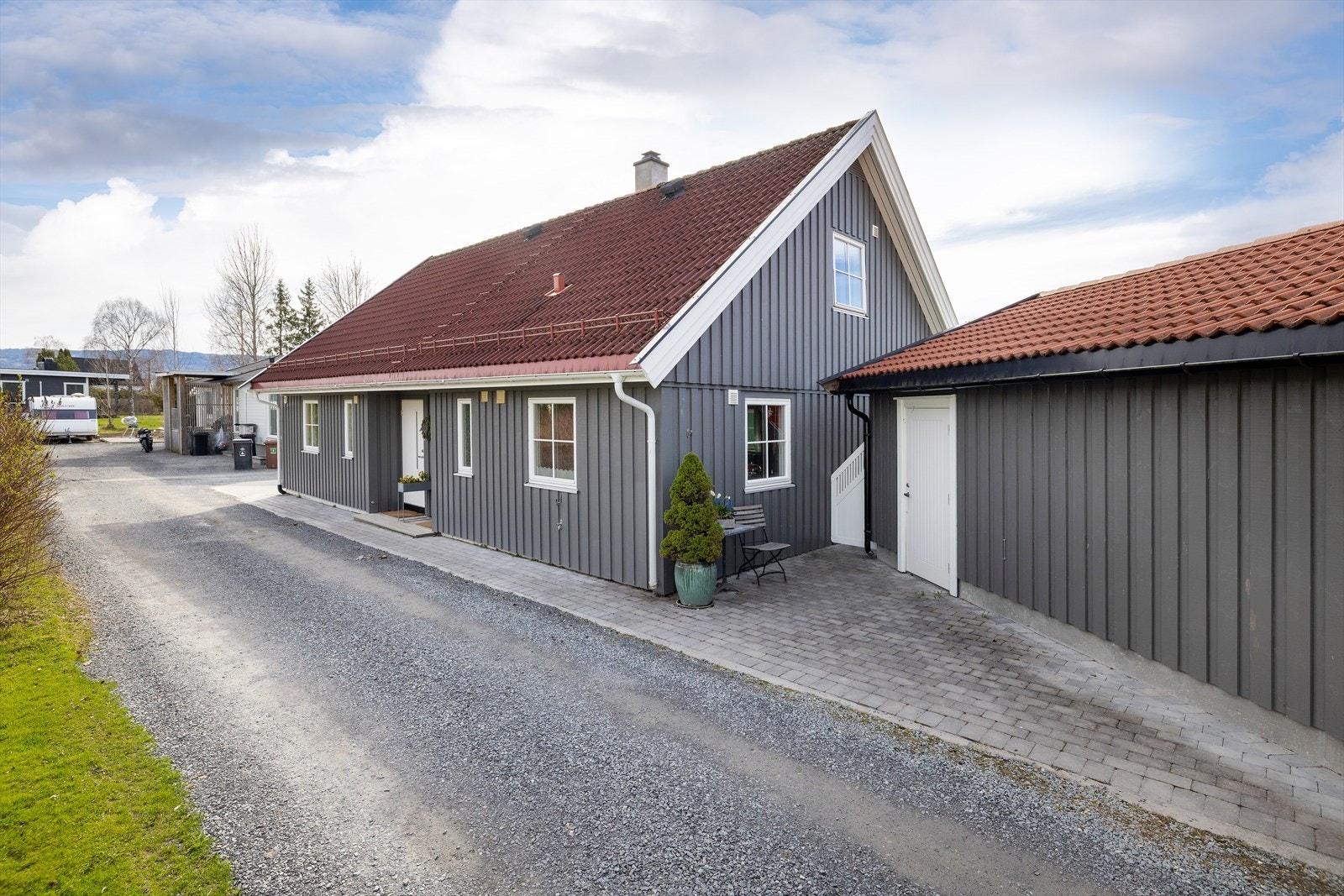 Eiendommen har en lettstelt hage og gruset innkjørsel med belegningsstein fremfor garasje og inngangsparti samt , inn mot hagesiden og på parkering for utleiedel. Galleribilde