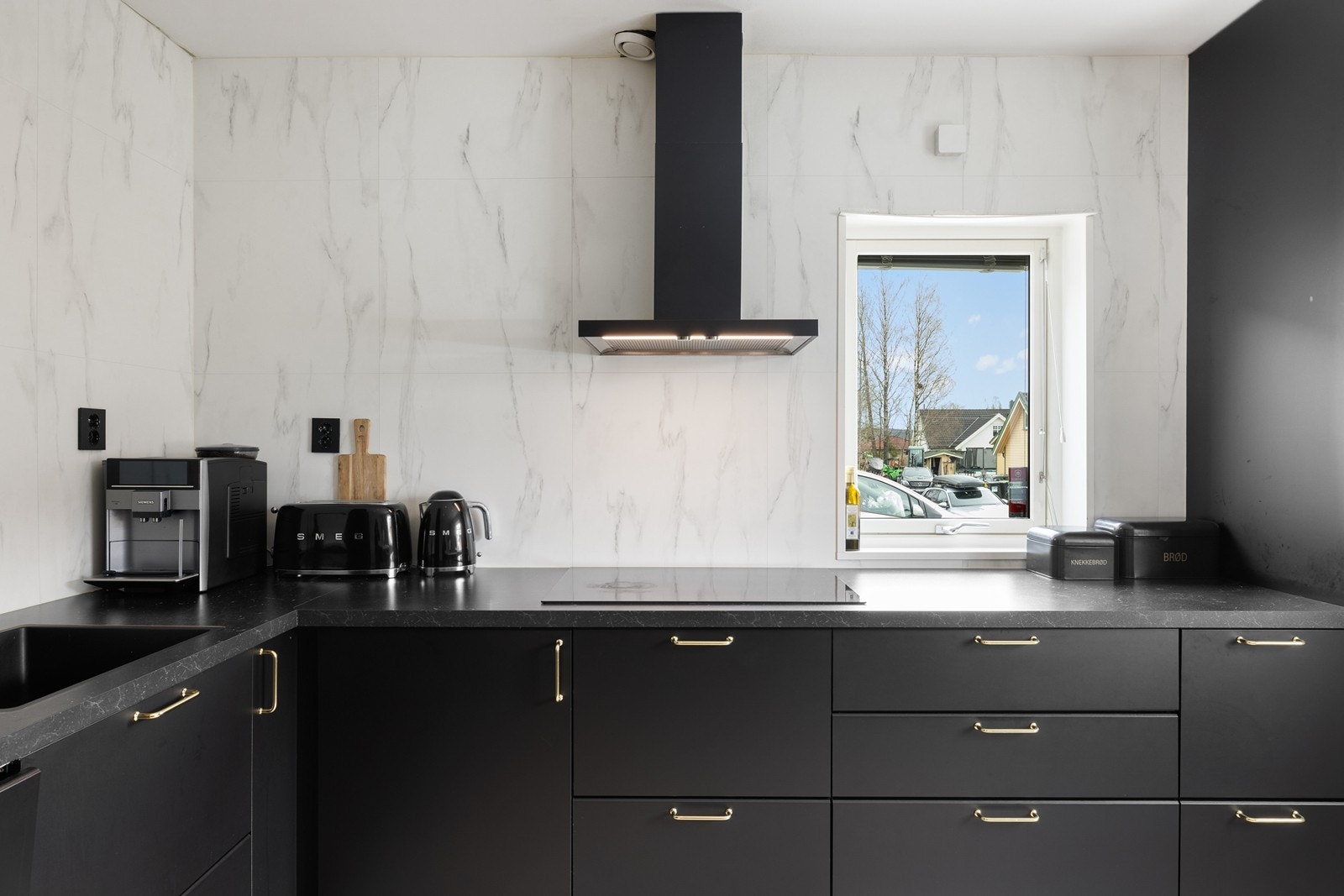 Den lyse benkeplaten med marmor-mønster skaper en lekker kontrast til de mørke, moderne frontene med elegante detaljer i gull/messing. Galleribilde