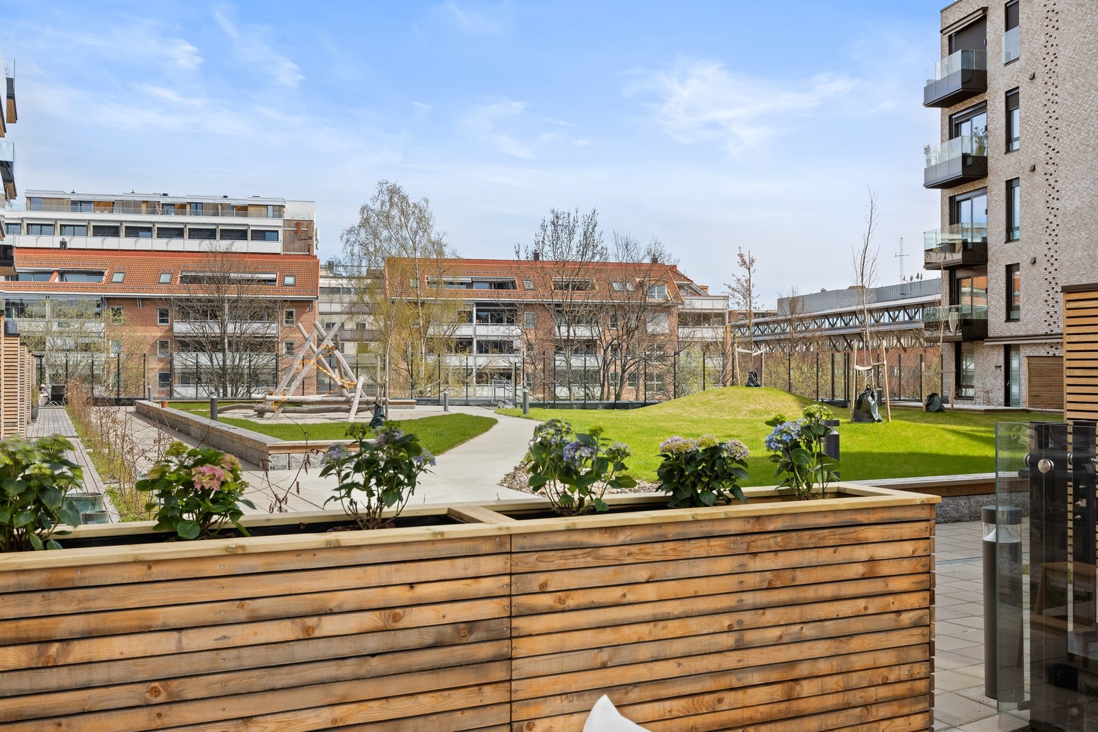 Utsikt mot fellesareal med lekeplass og grøntområde, omgitt av moderne leilighetsbygg. Galleribilde