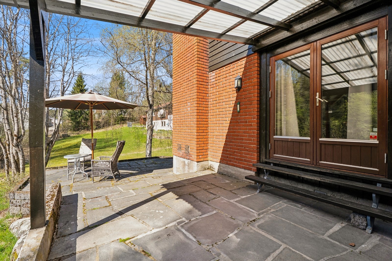 En tofløyet dør fra stuen åpner opp mot den store, skiferbelagte uteplassen med overbygget pergola. Galleribilde