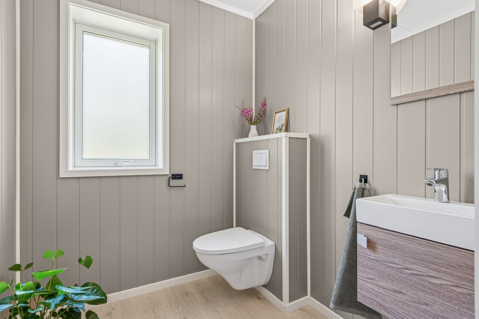 Separat toalettrom med vegghengt toalett og servant med underskap. Rommet har laminatgulv med gulvvarme, panelplater på veggene og himlingsplater i taket. Galleribilde