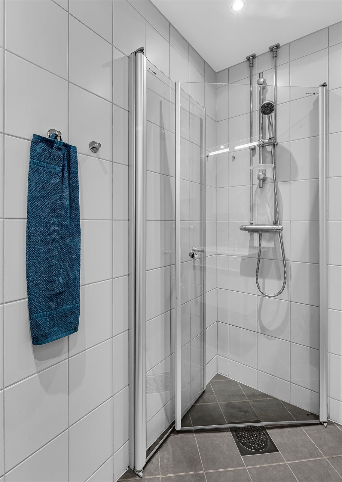 Badet er utstyrt med dusjhjørne med glassdører og dusjgarnityr, vegghengt toalett samt baderomsinnredning med skuffer, heldekkende servant og ett-greps blandebatteri. Galleribilde