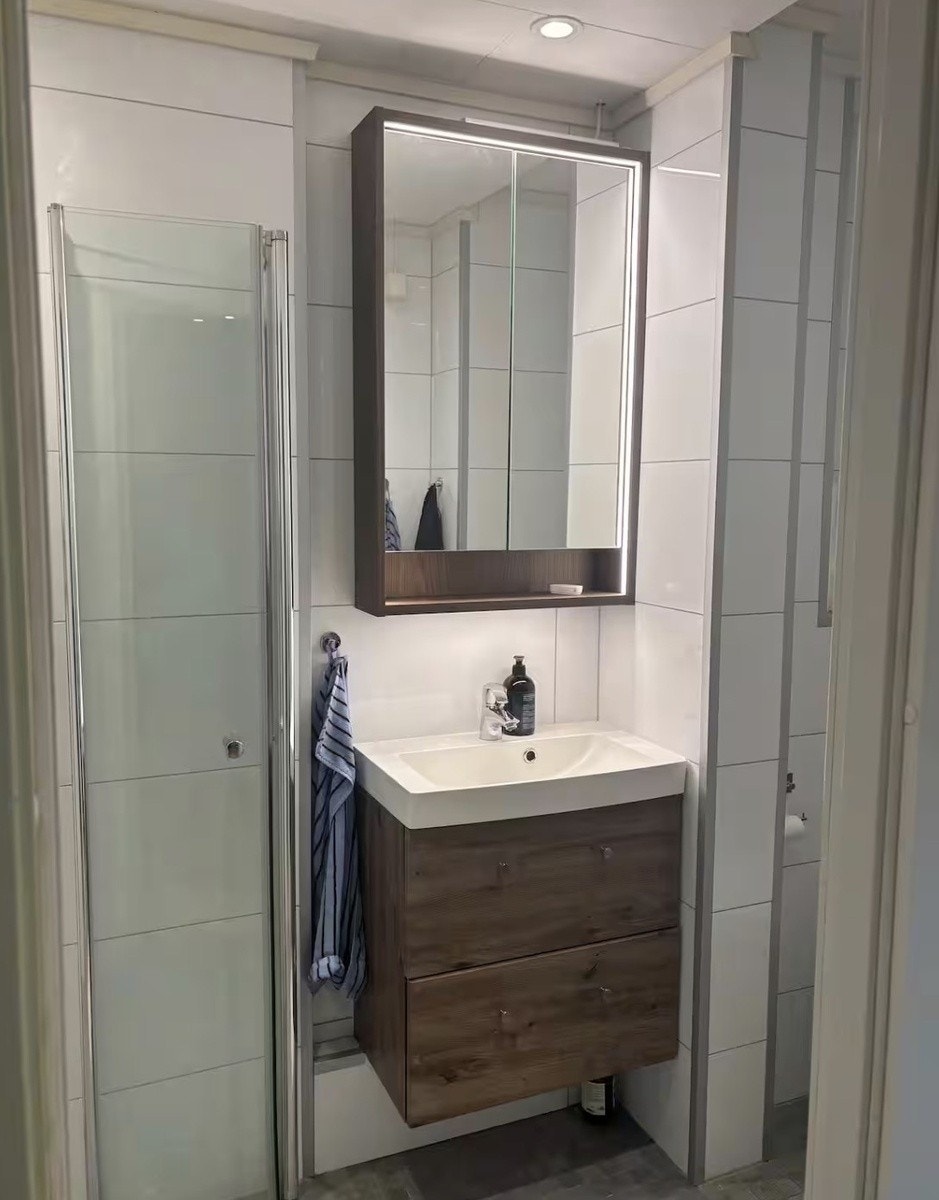 Badet er utstyrt med dusjhjørne med innfellbare dusjdører, gulvvarme, servant med skap, vegghengt toalett og speilskap. Galleribilde