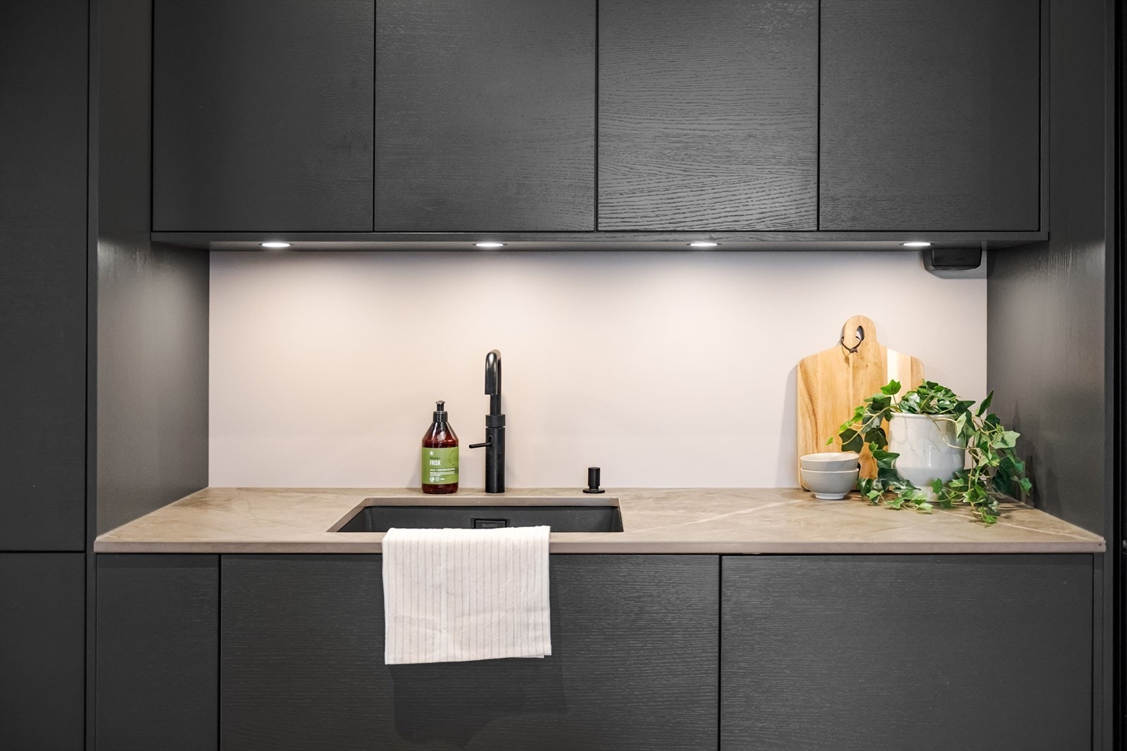 Innredningen har fine mørke fronter og påkostet benkeplate av kompositt med underlimt oppvaskkum og armatur med Quooker. Praktisk med innfelt belysning under overskapene. Galleribilde