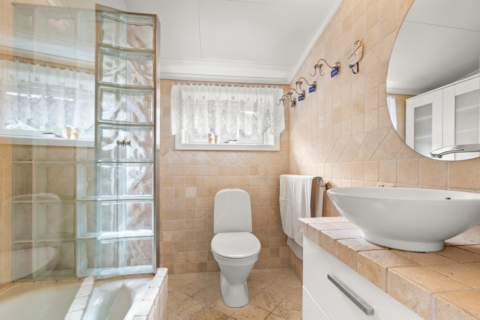 Badet er flislagt og har både dusj i badekar og innredning med speil, belysning og høyskap. Det er varme i gulvet og ventilasjon via elektrisk vifte og luftespalter. Galleribilde