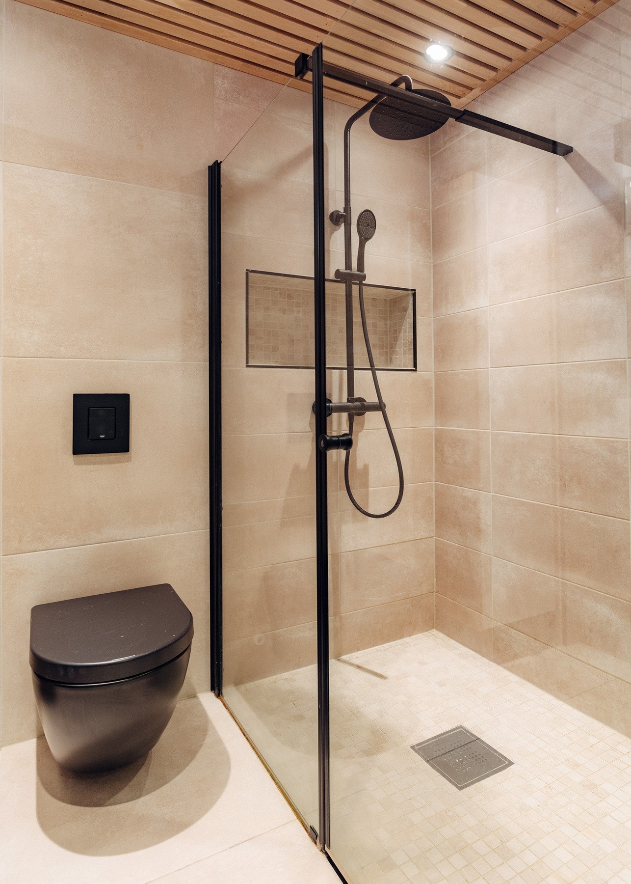 Rommet har flislagte gulv med varmekabler. Videre er badet utstyrt med dusjnisje med glassdør og integrert hyllesystem, servant med innredning, og vegghengt wc. Galleribilde
