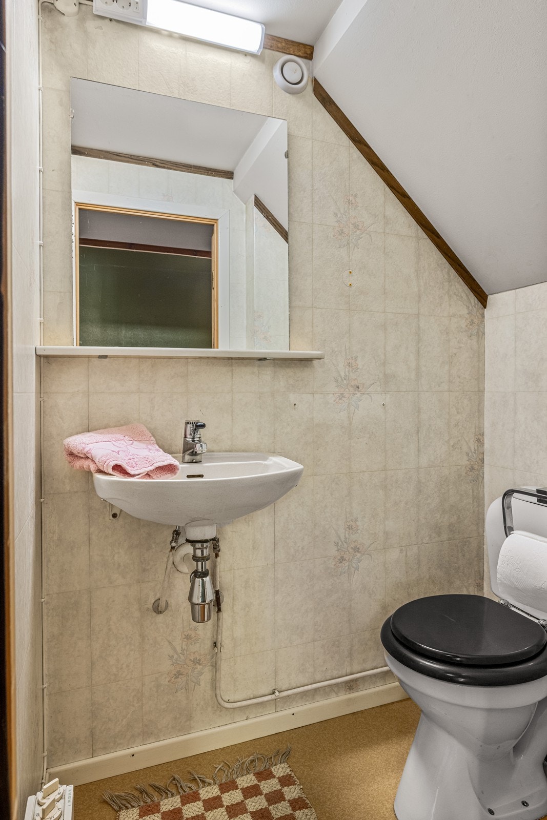 Praktisk toalettrom i underetasjen, plassert under trappen, med en standard fra byggeåret. Utstyrt med WC og servant. Galleribilde