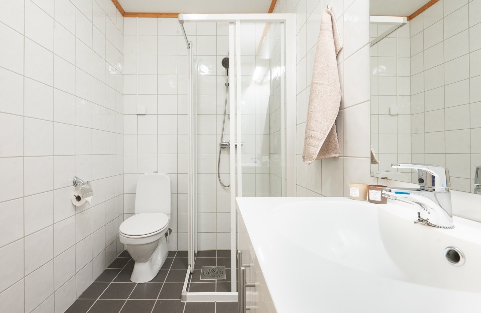 Badet har en funksjonell utforming med grå fliser på gulv og hvite fliser på vegger. Varmekabler i gulvet gir økt komfort året rundt. Galleribilde