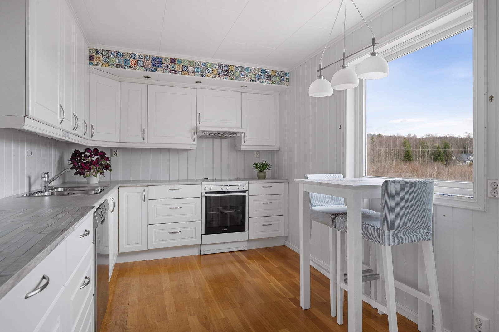 Kjøkkeninnredningen har hvite, profilerte fronter, laminert benkeplate og en praktisk frokostplass ved vinduet. Galleribilde