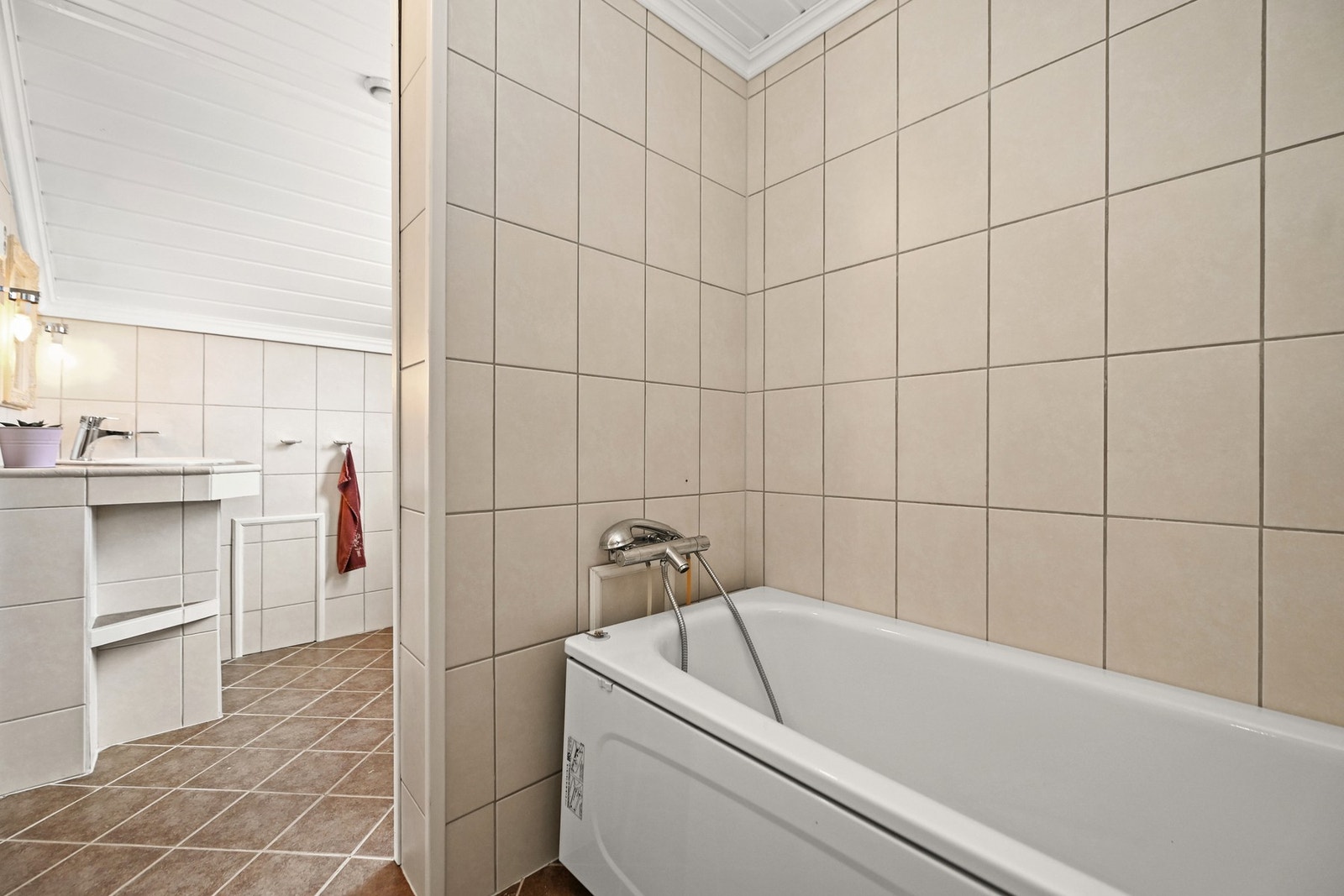 Badet har flislagte vegger og gulv, med badekar og servant. Galleribilde