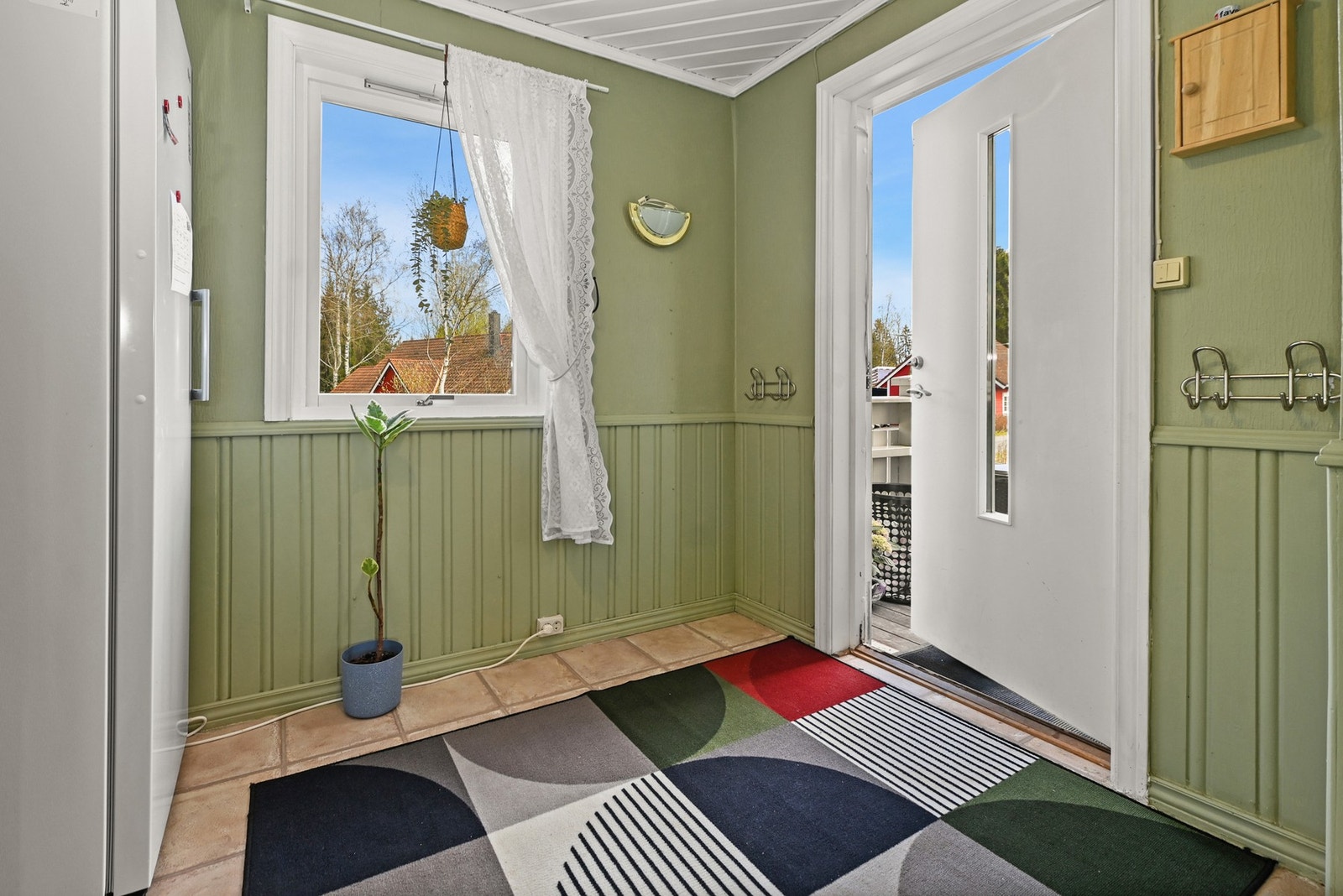 Lyst rom med grønn panelvegg, flislagt gulv og vindu med utsikt til hage. Galleribilde