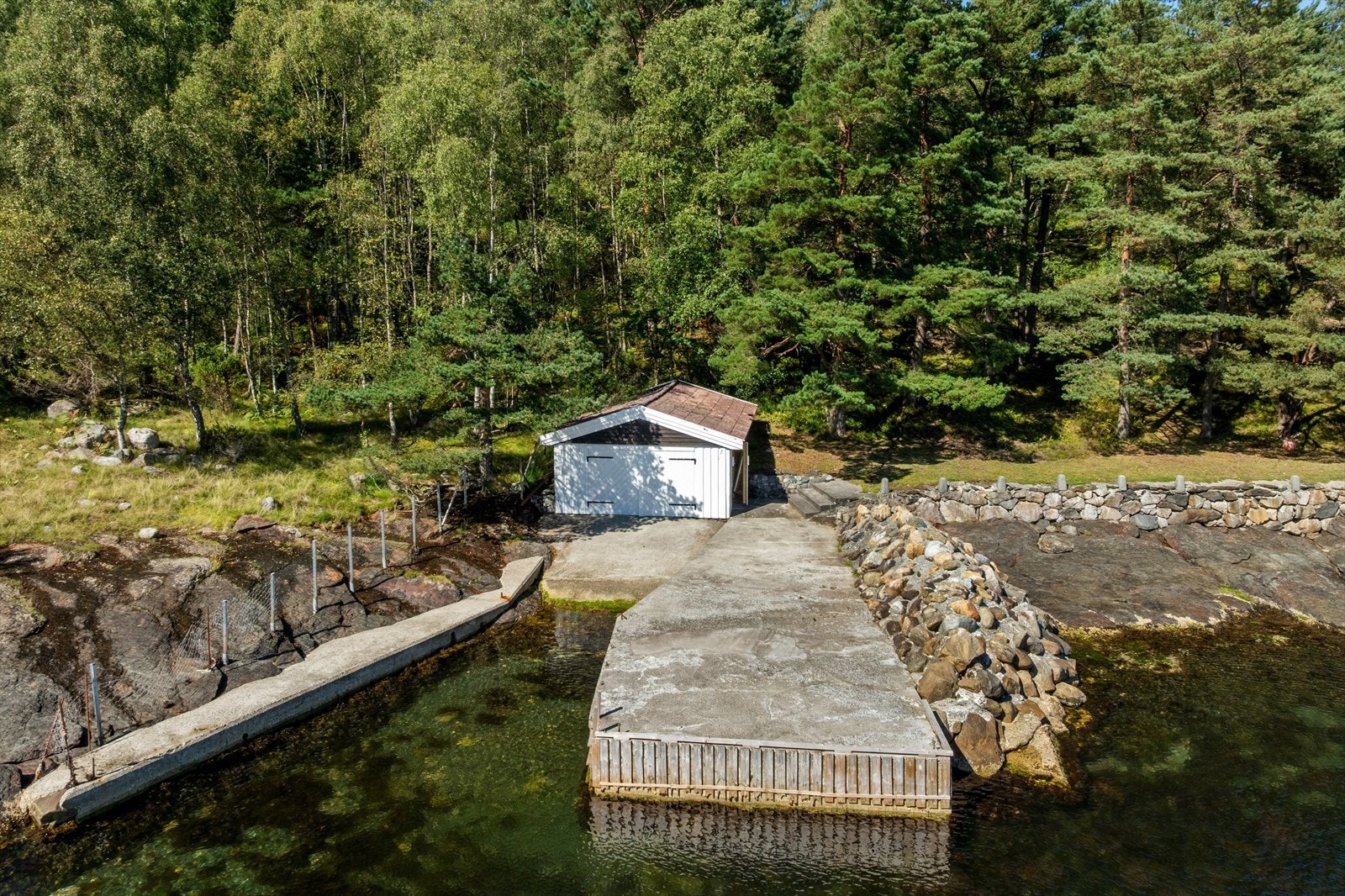 Naust med båtopptrekk og støpt kai i hjørnet av tomta. Galleribilde