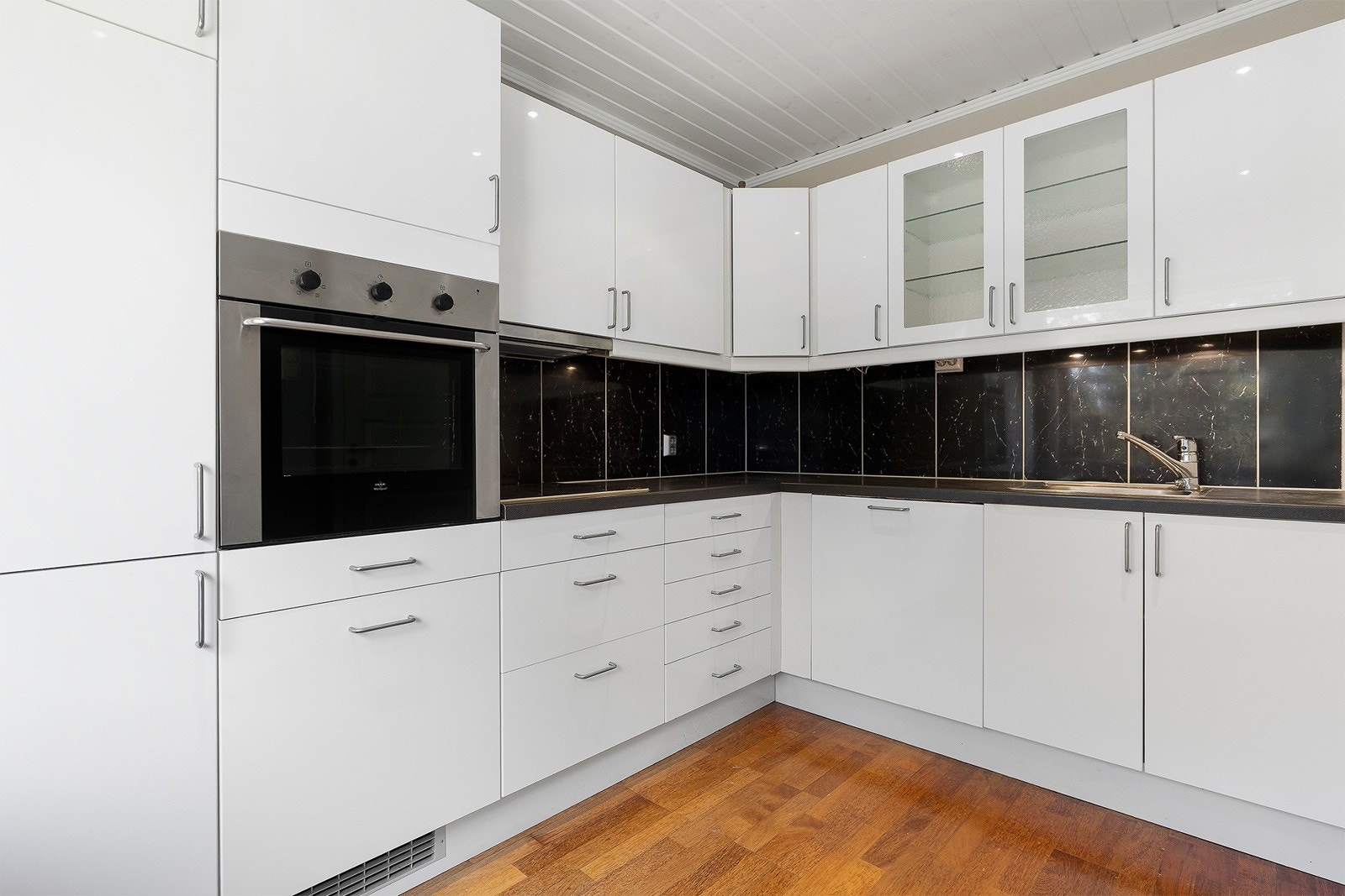 IKEA-kjøkkeninnredning med glatte høyglans skapfronter, laminat benkeplate med fliser på bakvegg, enkel oppvaskkum, ventilator og innfelte hvitevarer som koketopp, stekeovn, oppvaskmaskin, kjøl/- fryseskap. Galleribilde