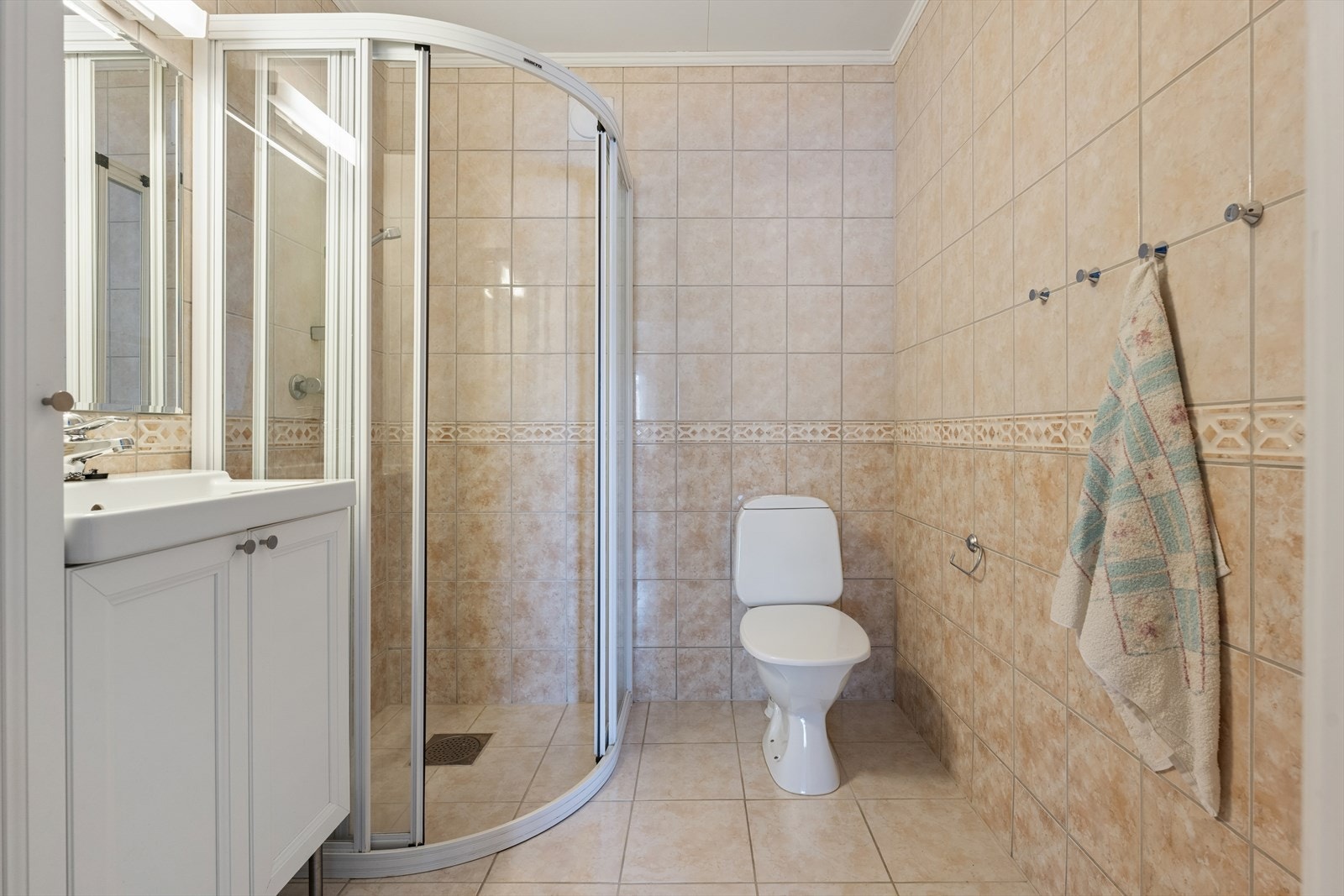 Baderommet i underetasjen er innredet med beige, sjatterte fliser på gulv og vegger. I gulvet har man også varme for ekstra komfort. Badets grunnbase er fra byggeår, men er modernisert i senere tid med fliser. Galleribilde