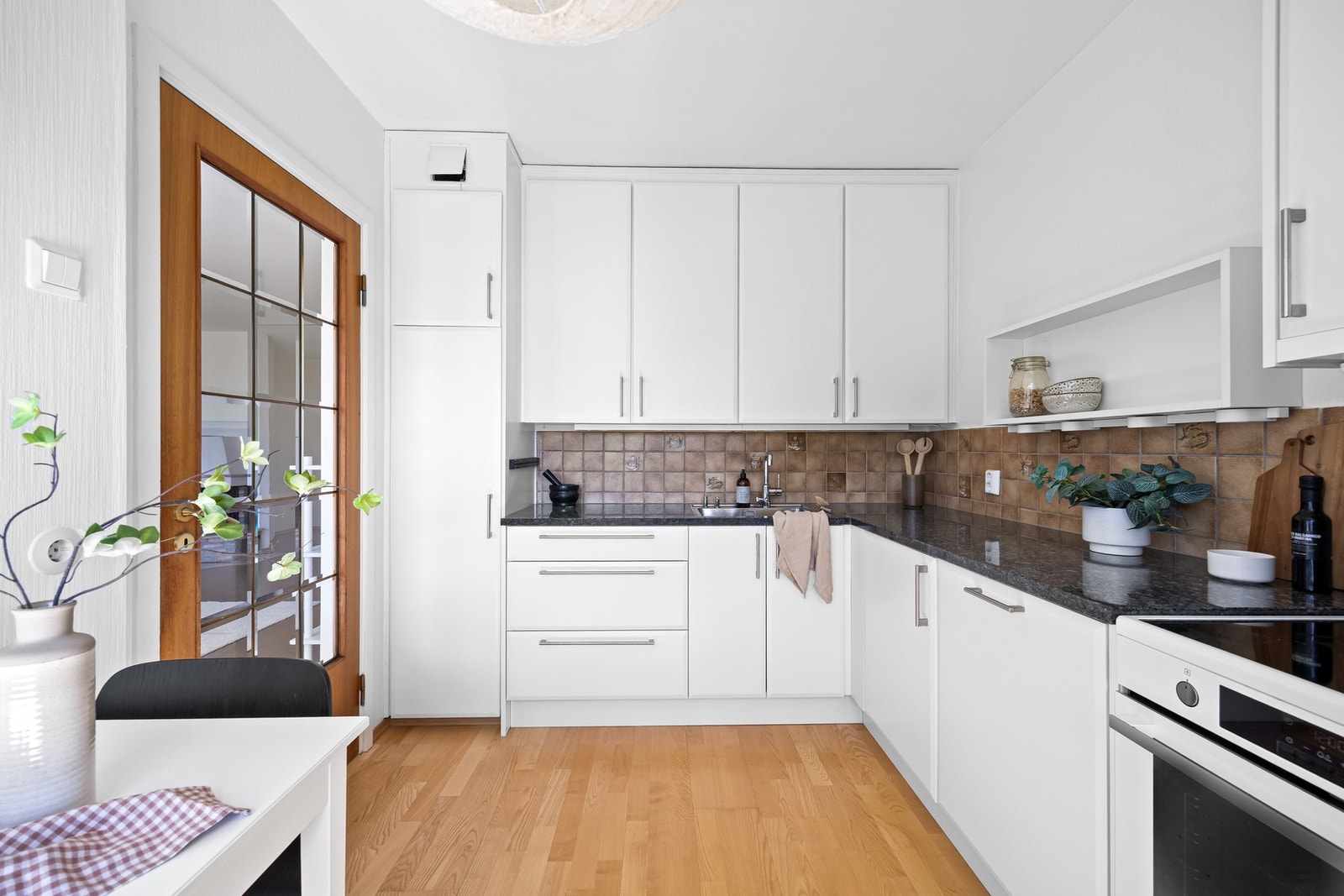 Kjøkkeninnredning med glatte fronter, benkeplate i larvikitt med høy slitestyrke og nedfelt kum i rustfritt stål. Fliser på vegg over benkeplate. Fronter og benkeplate ble byttet ut i 2016. Galleribilde