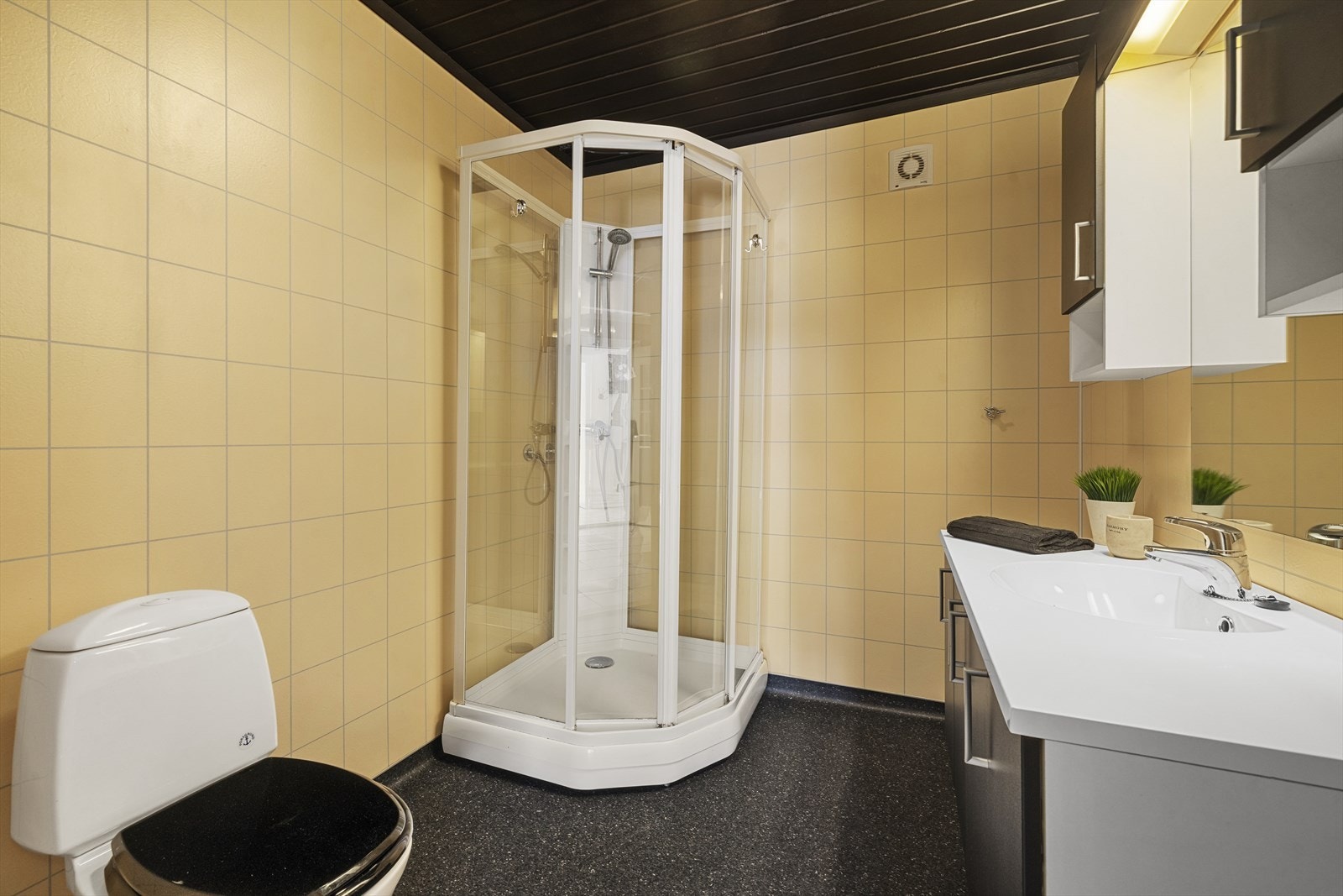 Badet har belegg på gulv og fliser på vegger. Baderommet er utstyrt med servant over skapinnredning, speil med overliggende belysning, sideskap, dusjkabinett og toalett Galleribilde