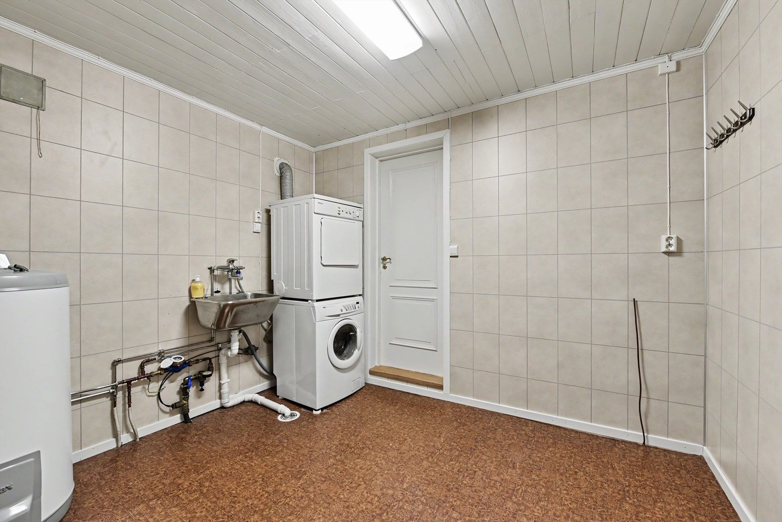 Romslig vaskerom i underetasjen med gulvbelegg og baderomsplater på veggene. Her er det opplegg for vaskemaskin og utslagsvask. Galleribilde