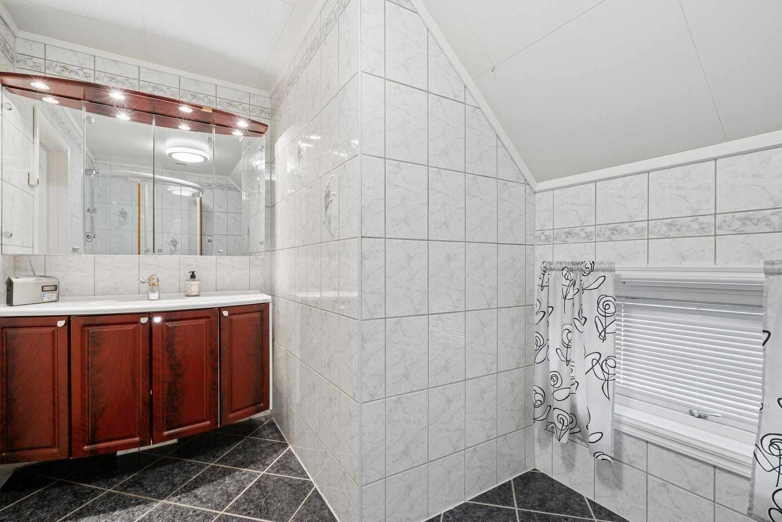 Badet er innredet med dusjhjørner, toalett, vask, baderomsinnredning og speilskap. Galleribilde