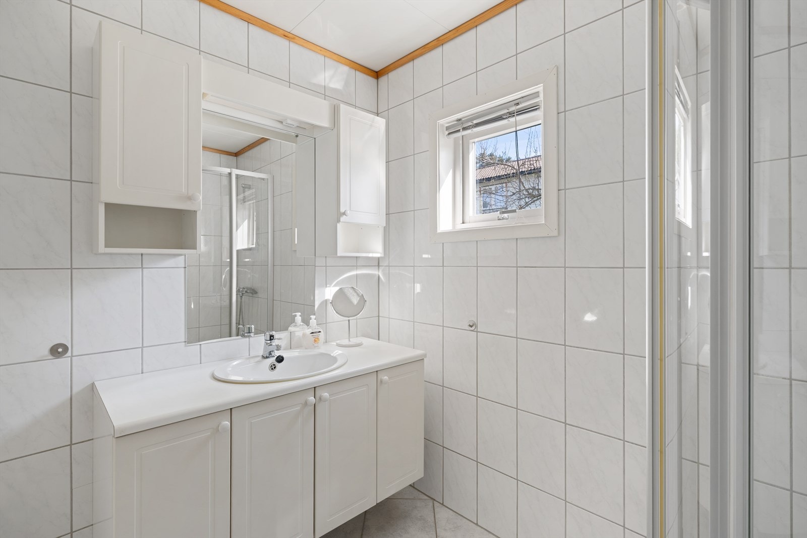 Badet er utstyrt med innredning med servant og overskap med speil. Dusj med dusjdører av glass og dusjgarnityr på vegg samt gulvmontert toalett Galleribilde
