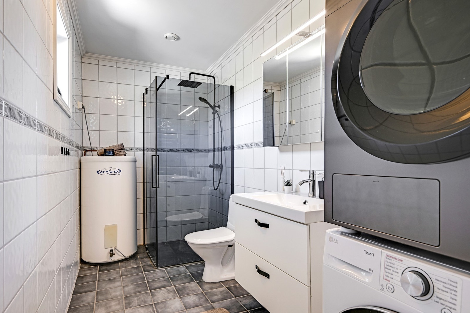 Badet har dusjhjørne, toalett, servant med underskuffer, vaskemaskin og tørketrommel. Det er flislagte vegger og gulv, og mekanisk avtrekk Galleribilde