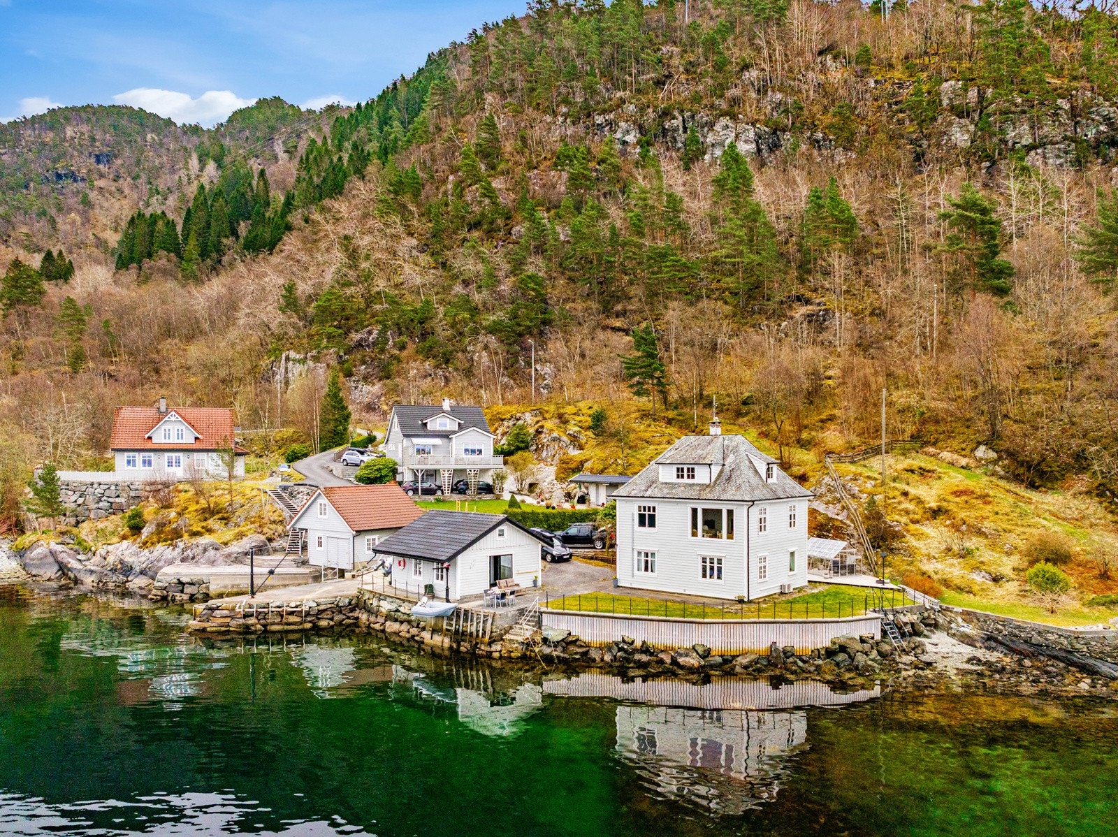Vestvendt bolig ved sjøen med fjell i bakgrunnen. Klar vannflate og frodig natur. Galleribilde