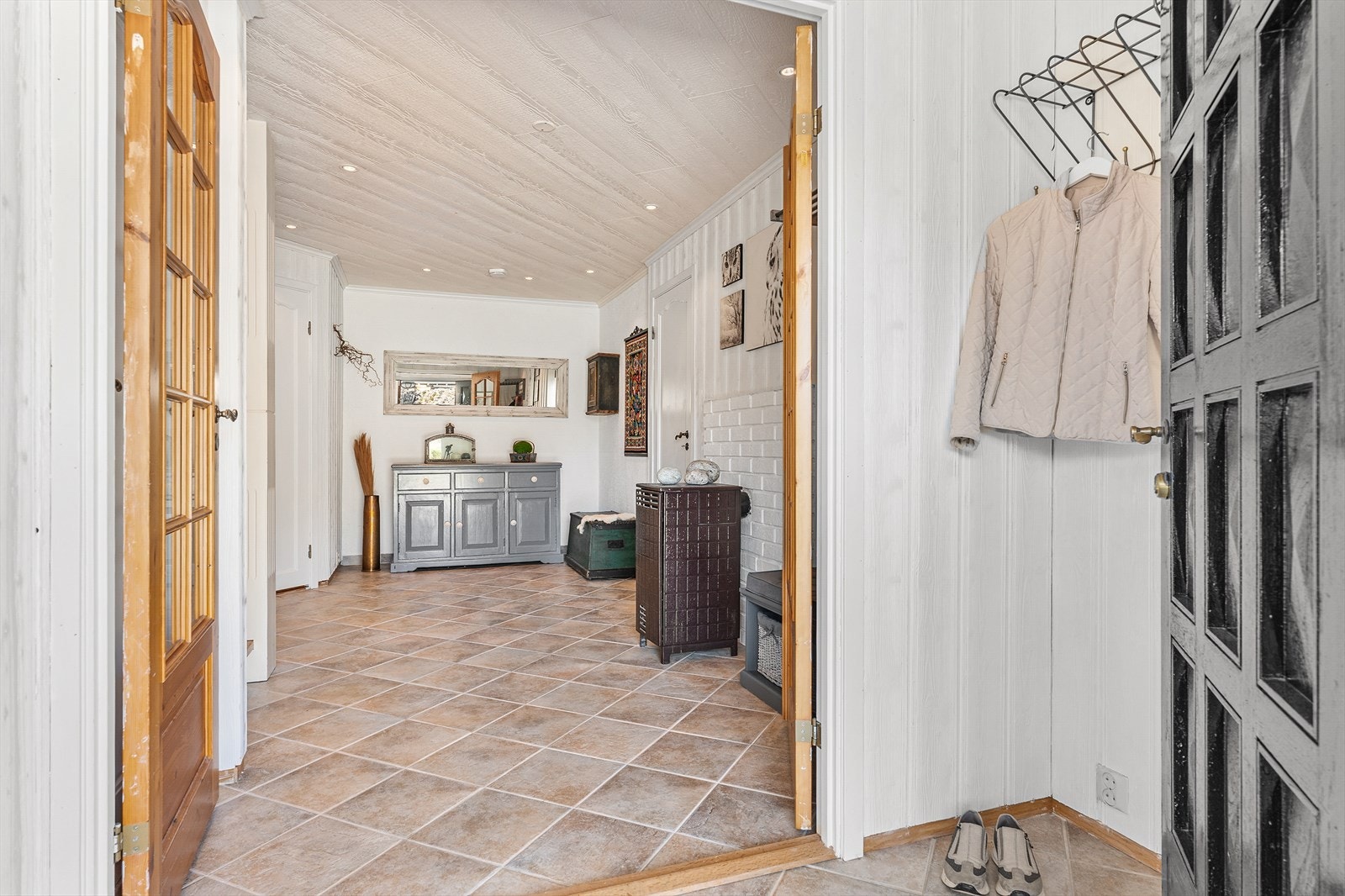 Hovedinngangen til boligen leder inn i en romslig entré med vedovn og flislagt gulv med varmekabler. Galleribilde